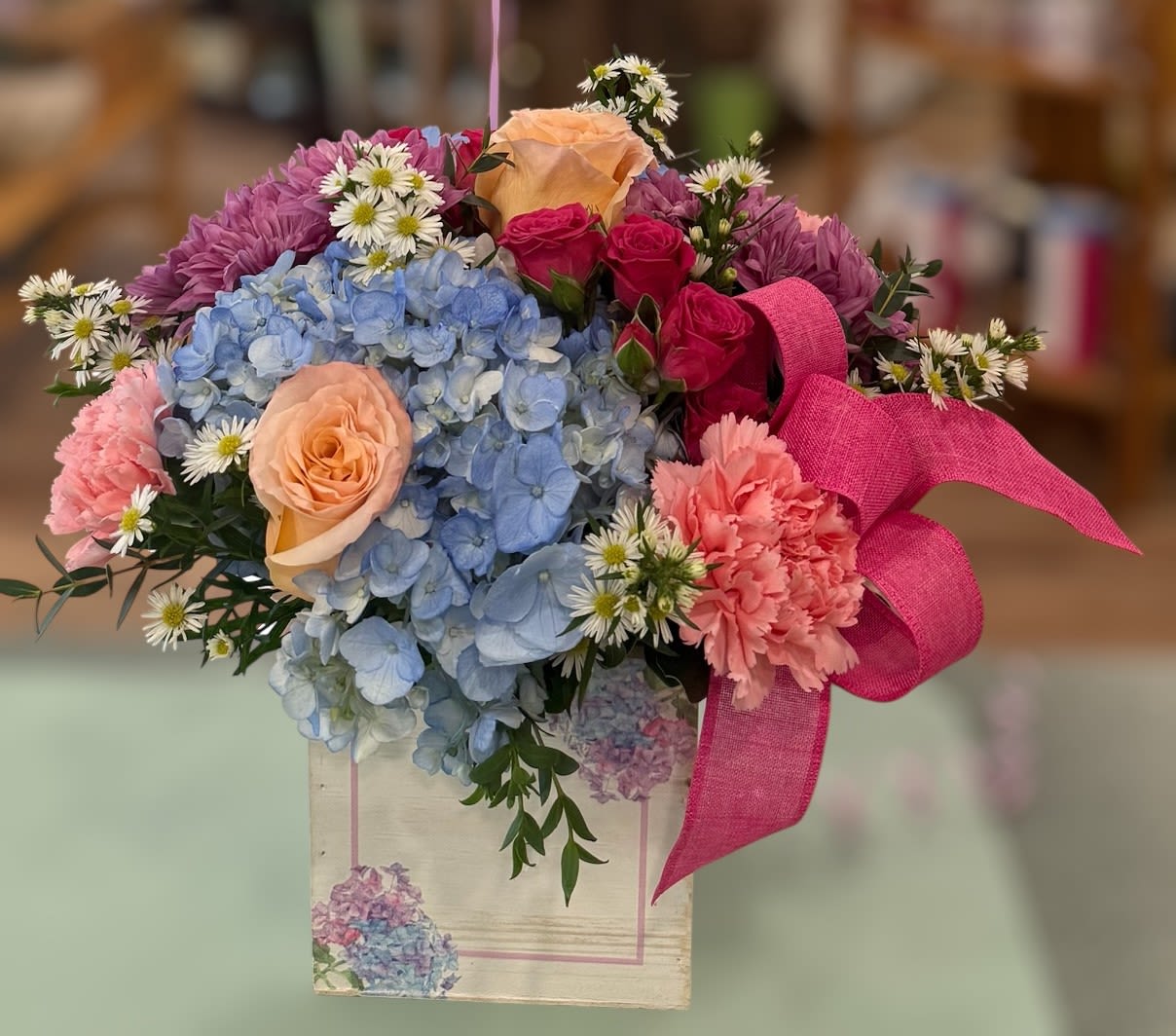 Hydrangea Bliss with a Mother's Day Balloon (HYB) - A mix of blue hydrangeas, peach roses, pink spray roses, pink carnations, purple daisies and filler arranged snugly in a wooden decorative box with a vivid pink ribbon and Mother's Day Balloon. The perfect gift for Mother's Day.  ***Flower color may vary depending on availability. 
