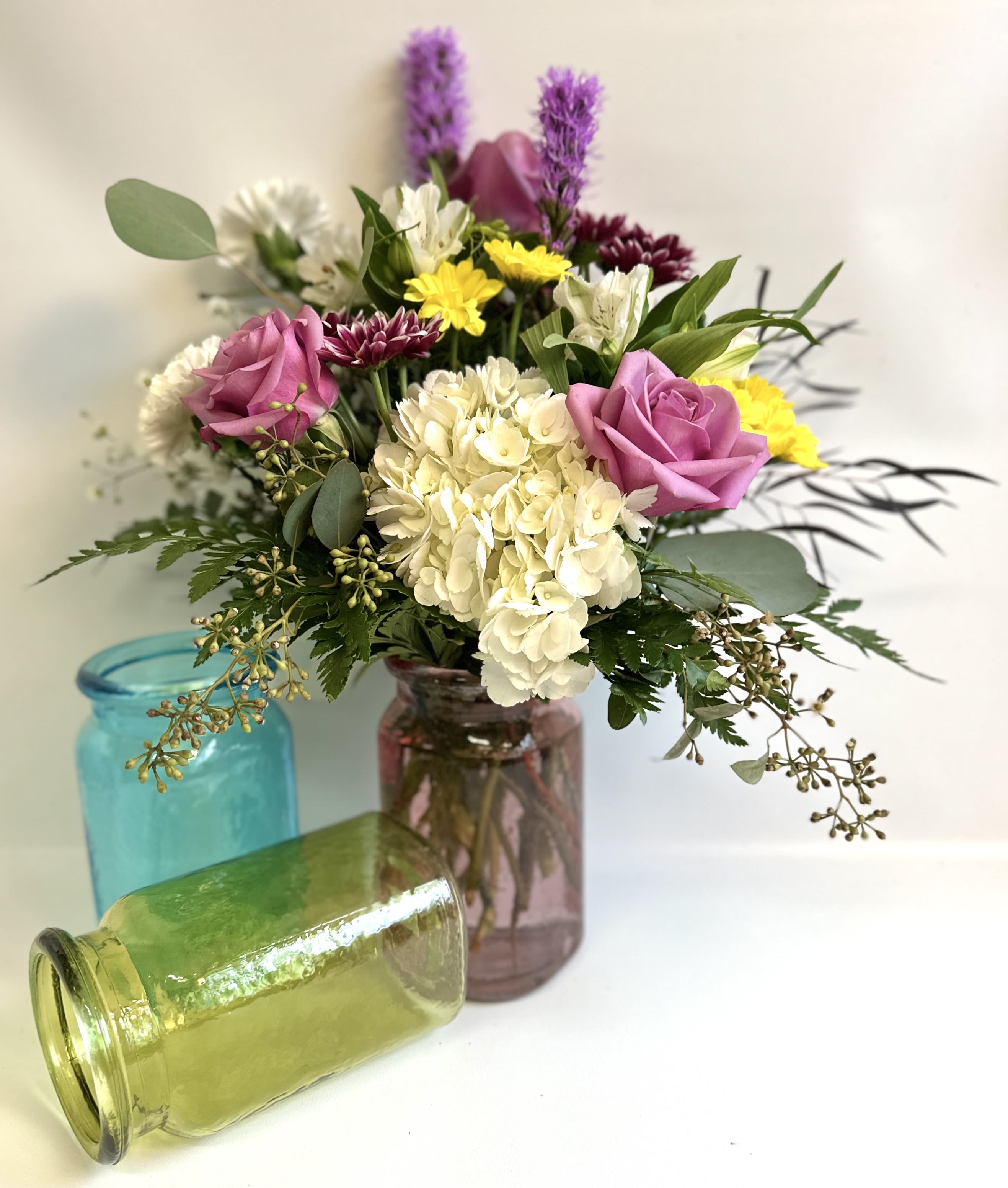 Mixed bouquet in colorful glass jars with pink roses and white hydrangea