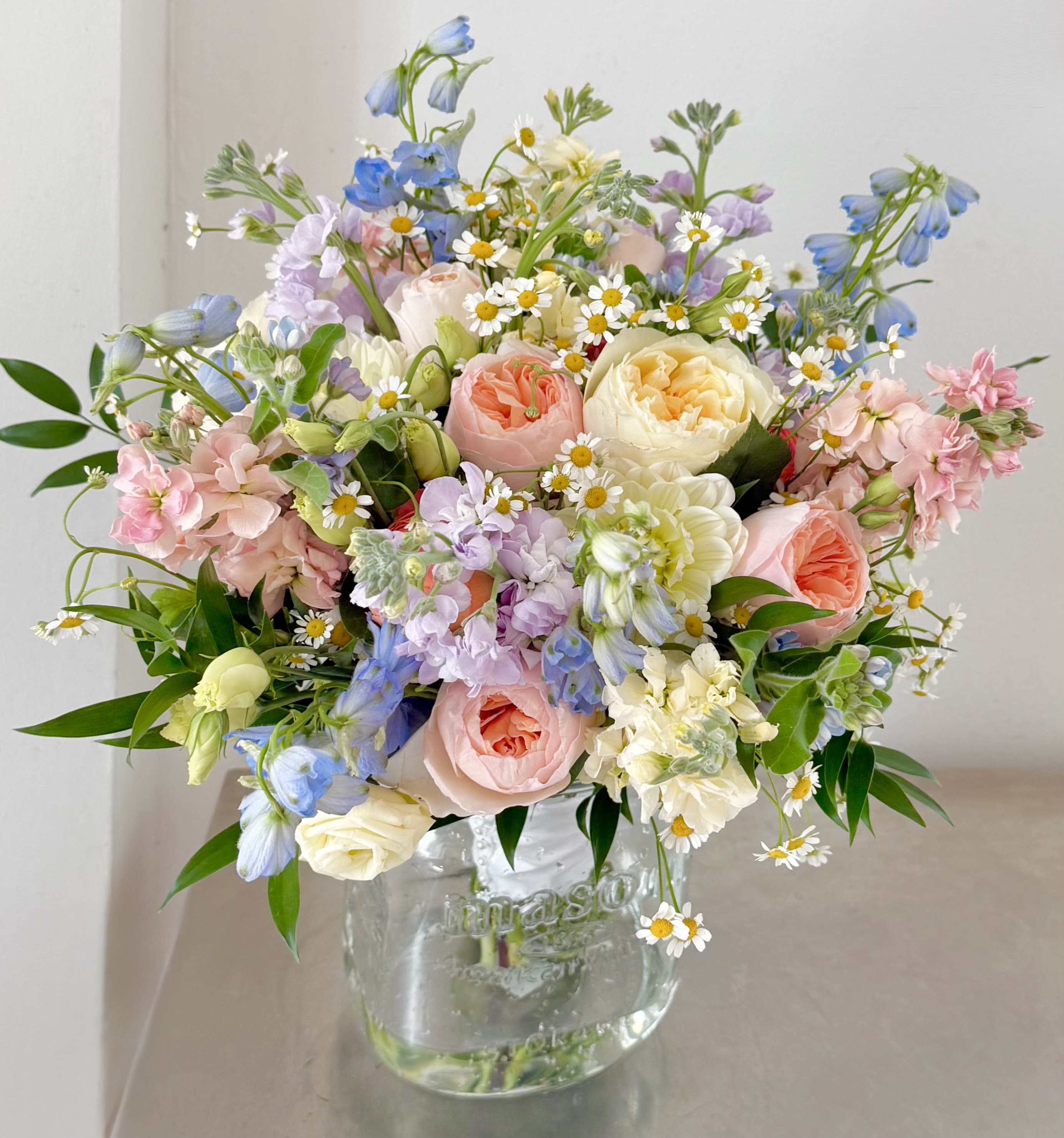 Georgetown Garden Bouquet - A romantic, garden-gathered bridal bouquet inspired by the soft charm of a spring morning in Washington, DC. This design blends heirloom garden roses in blush, peach, and buttercream with airy delphinium, and delicate chamomile daisies for a bouquet that feels freshly picked from an English garden.  Loose, natural movement gives this bouquet an effortless elegance, while layers of pastel blooms and fresh greenery create depth, texture, and a timeless bridal look. The palette of powder blue, soft pink, ivory, and fresh green is perfect for garden weddings, estate venues, and classic DC celebrations.  Each bouquet is hand-crafted with premium seasonal blooms and styled to feel organic, light, and romantic — ideal for brides who love refined beauty without anything feeling overly structured.  Flowers may include: Garden roses, stock, delphinium, chamomile daisies, lisianthus, and seasonal greenery.  Perfect for: Garden weddings • Estate venues • Spring &amp; summer ceremonies • Romantic, classic bridal style