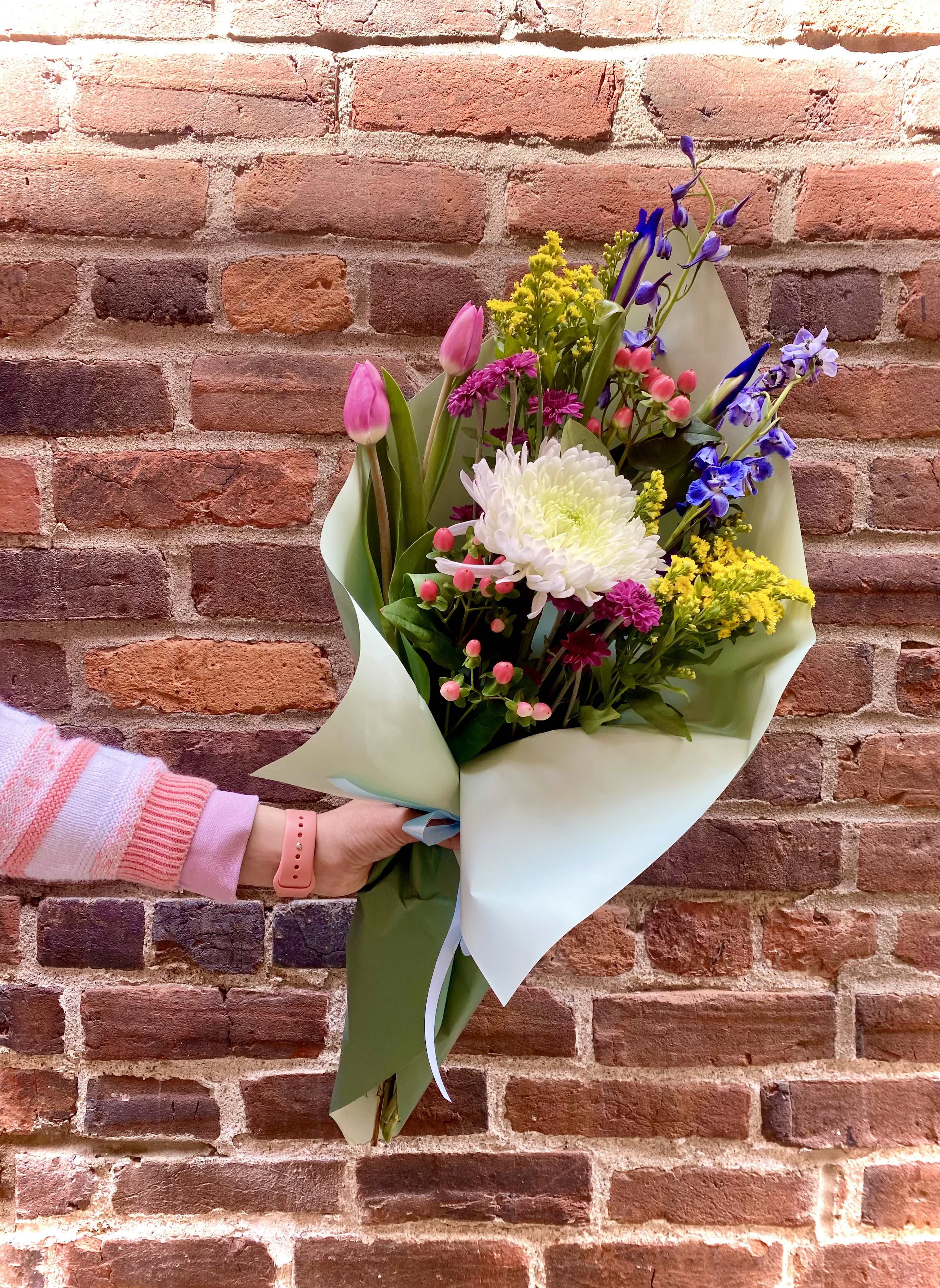 Handheld bouquet of pink tulips, white chrysanthemum, and purple flowers