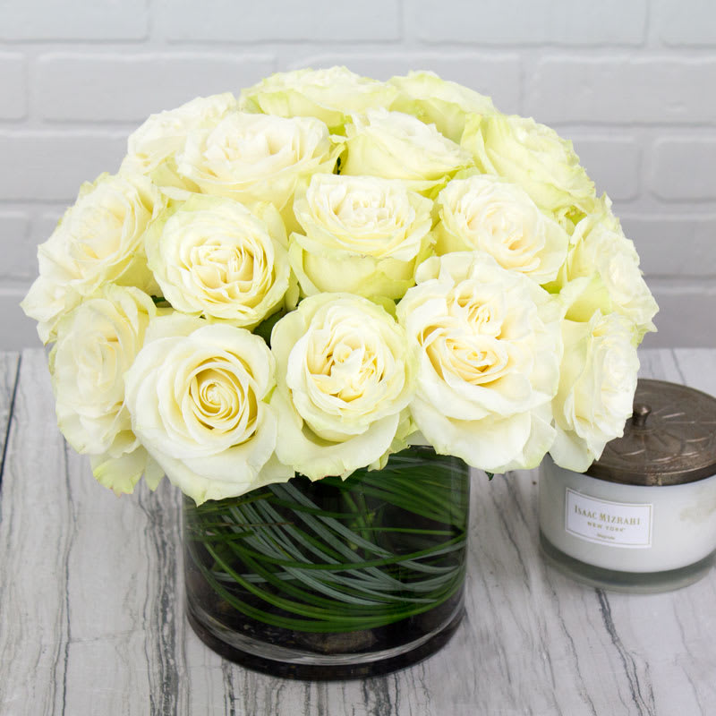 Bouquet of cream-white roses in a clear glass vase beside a candle jar