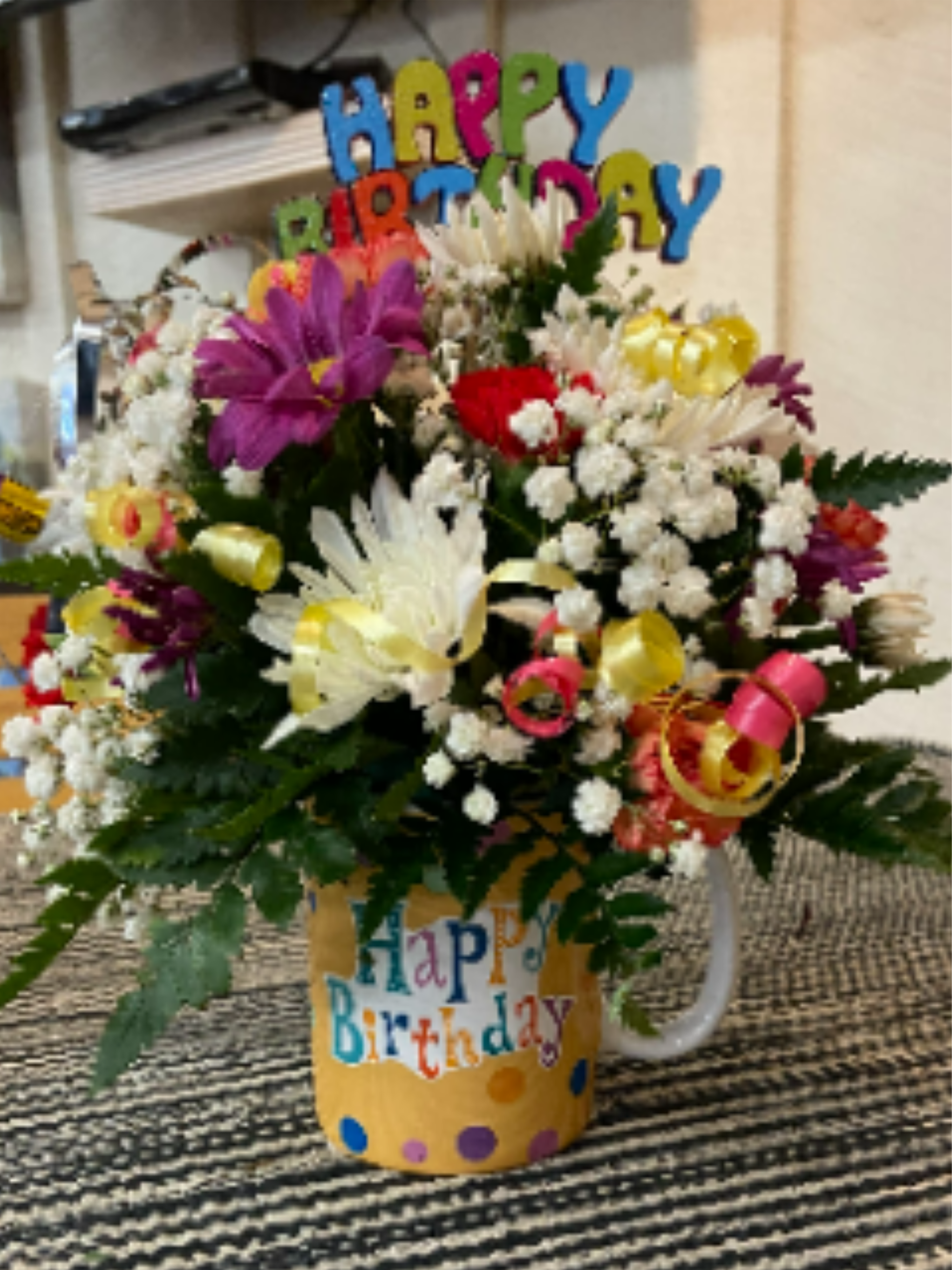 Birthday Mug - Time to celebrate with this super fun arrangement designed in a "Happy Birthday" mug filled with flowers in the colors of red, yellow, orange, and purple. Topped with ribbon, happy birthday picks, and party horns. 