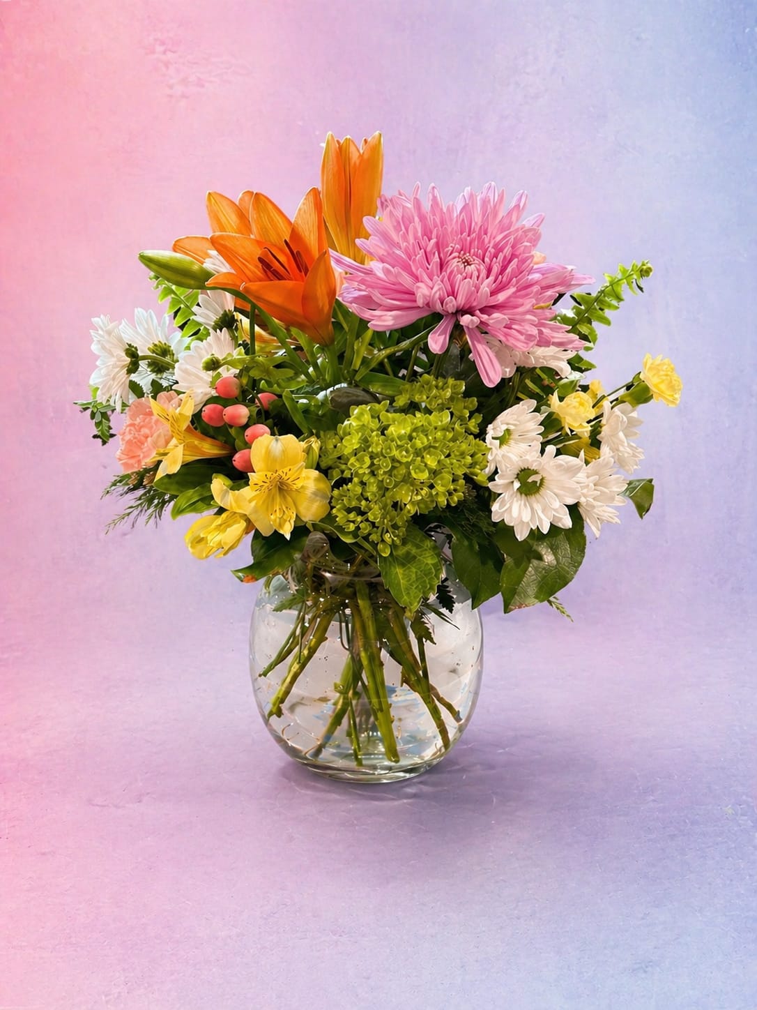 Sweet Sunshine Garden - A joyful mix of vibrant blooms designed to brighten any day. Featuring bold orange lilies, a soft lavender cushion mum, sunny yellow accents, and delicate white daisies, this arrangement brings together warmth and sweetness in one charming glass vase. Finished with fresh greenery and pops of texture.