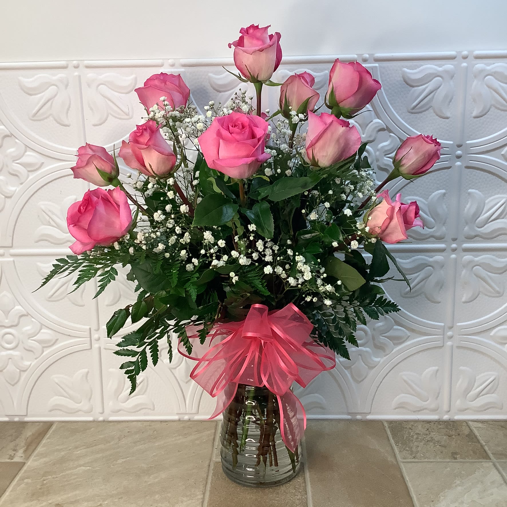 Pink roses arranged in a glass vase with baby's breath and a pink ribbon