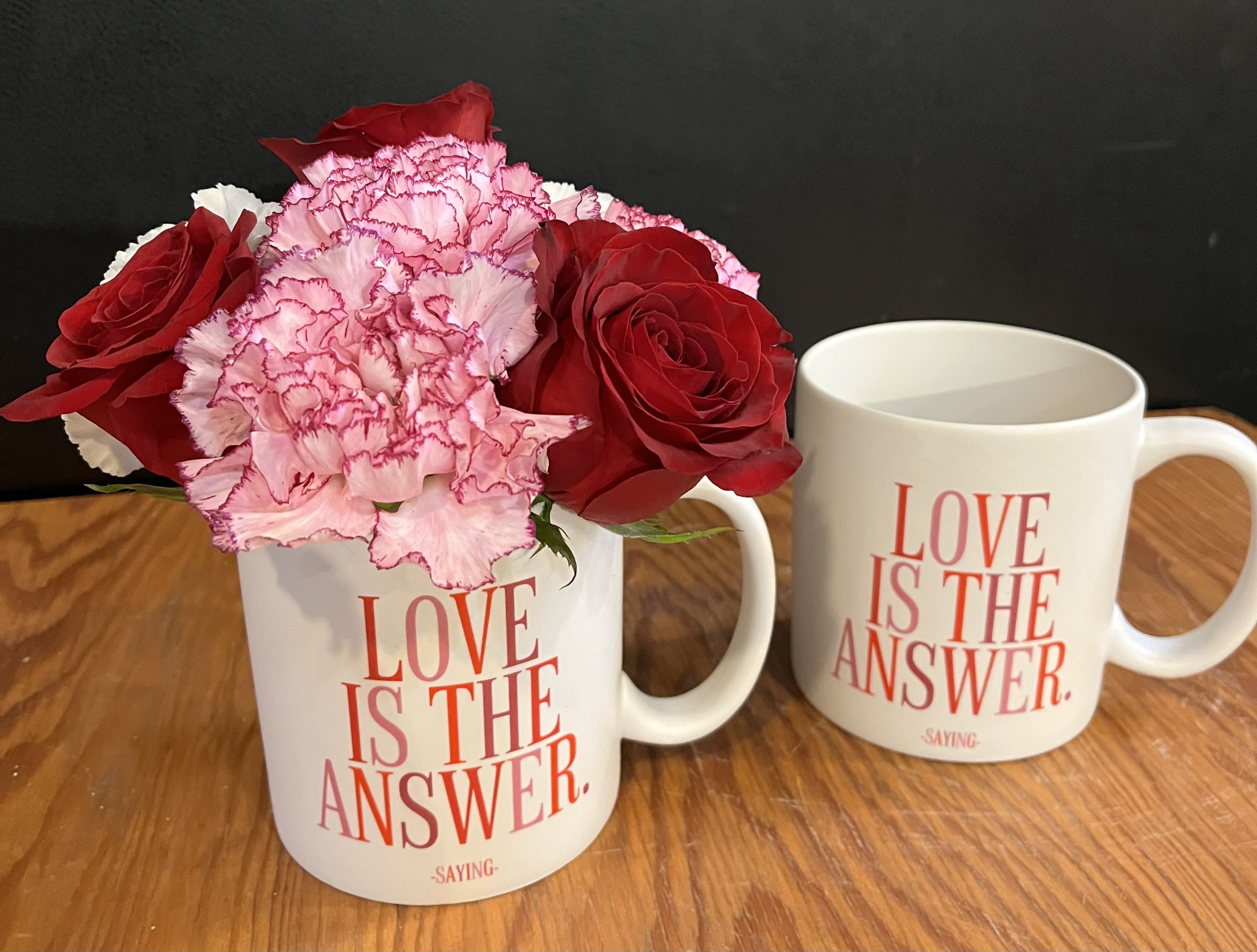 Red roses and pink carnations in a white mug beside a matching mug
