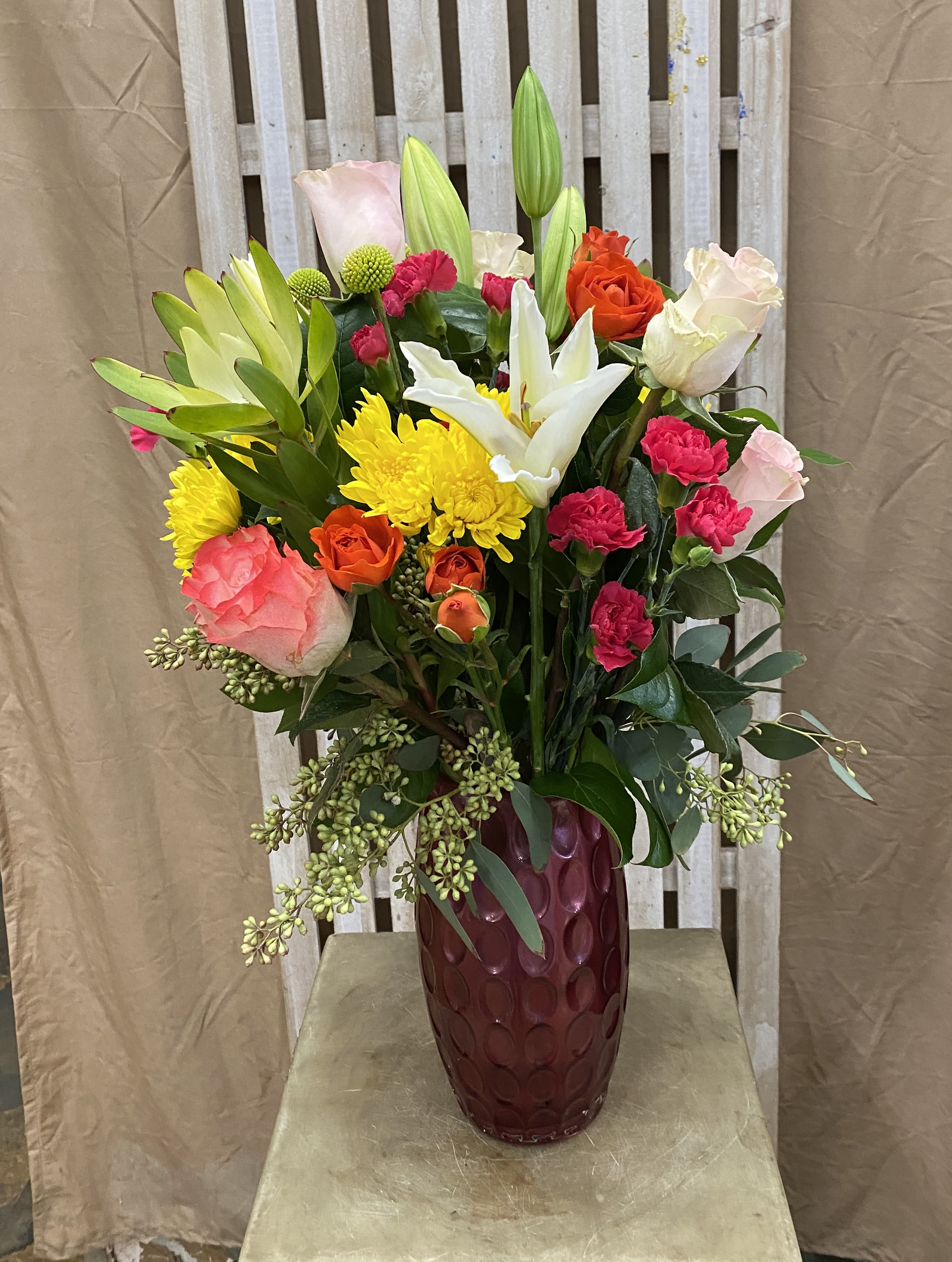 Mixed bouquet of roses, lilies, and chrysanthemums in a burgundy vase