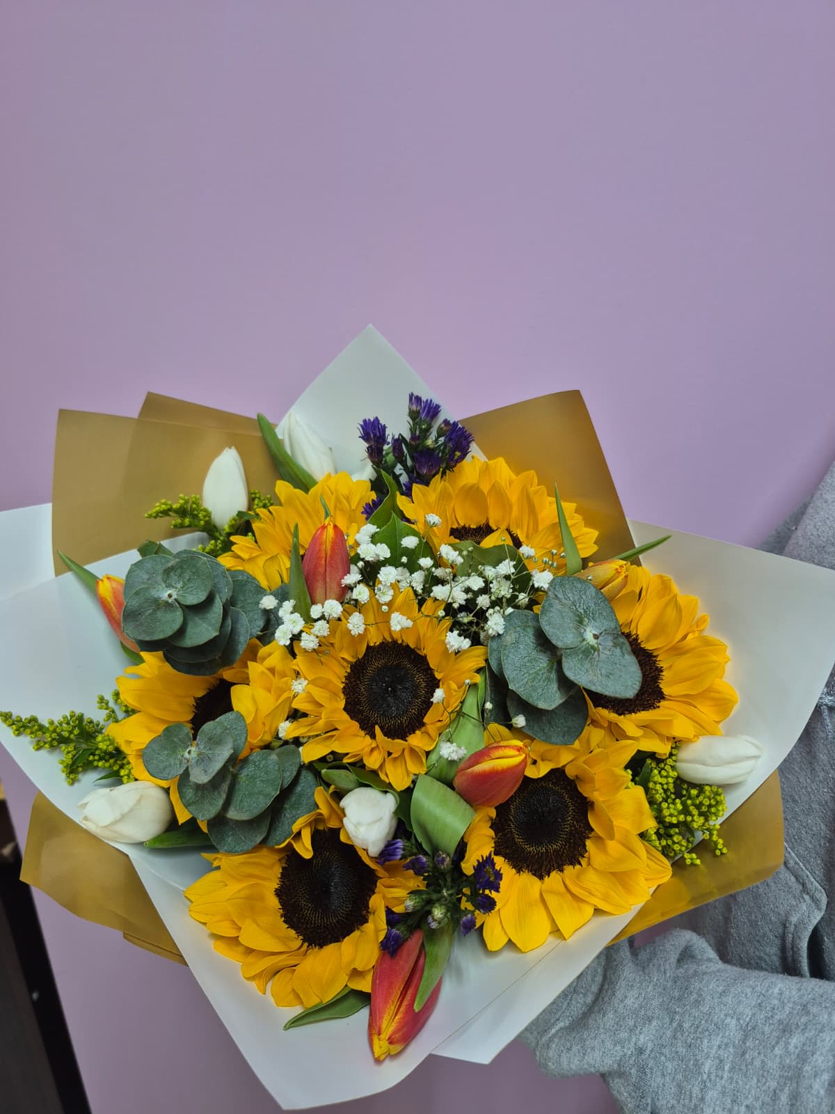 Bouquet of sunflowers, tulips, and white filler flowers wrapped in paper