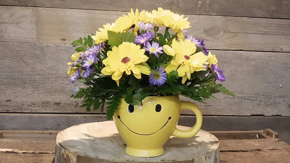 Yellow and purple flowers in a smiley-face mug vase