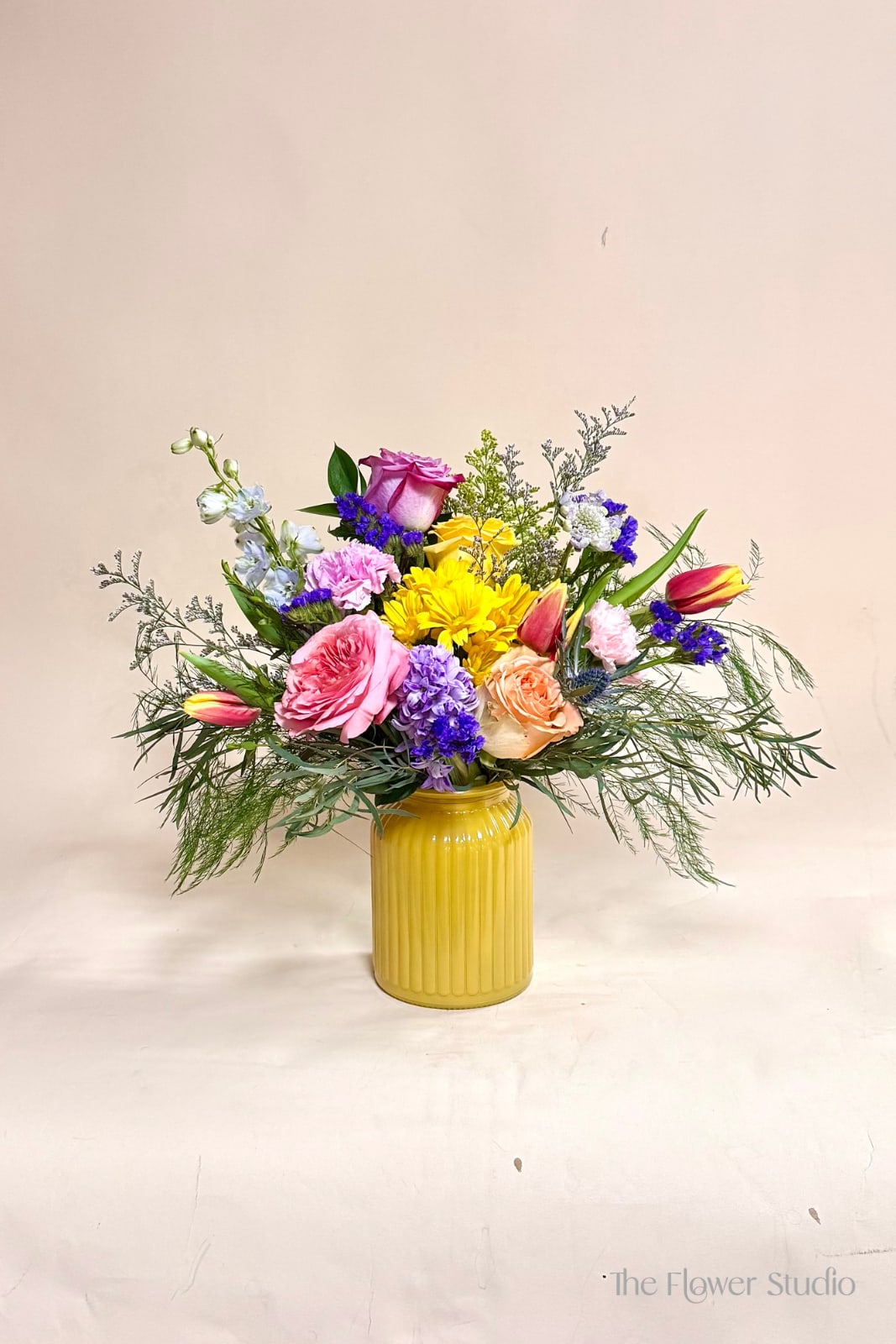 Colorful Love - A joyful, garden-style arrangement bursting with vibrant color perfect for Mother's day. Featuring soft pink and peach roses, sunny yellow blooms, and pops of purple and blue, this design is styled in a cheerful yellow vase with airy greenery for a fresh, natural feel. Perfect for brightening any space or celebrating life’s happy moments.