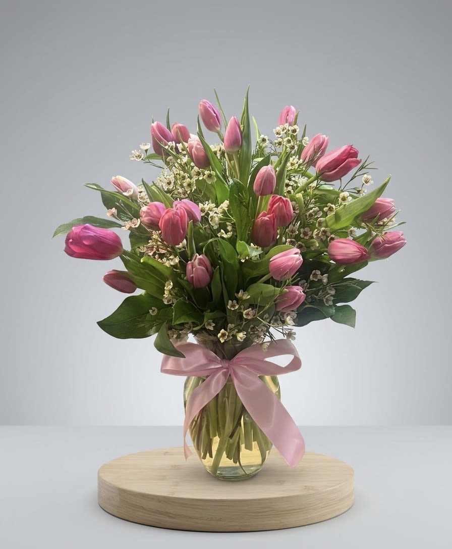 Tulip Delight - Our Pink Tulip &amp; Waxflower arrangement is a masterclass in garden-inspired design. Each vase is hand-styled with vibrant tulips that symbolize grace and affection, nestled among clusters of dainty waxflowers and lush, seasonal greenery. Finished with a signature satin ribbon, this arrangement is delivered ready to display—offering a sophisticated look that is perfect for a tabletop, desk, or mantle.