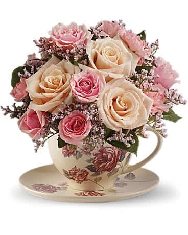 Pink and cream roses arranged in a floral teacup with saucer