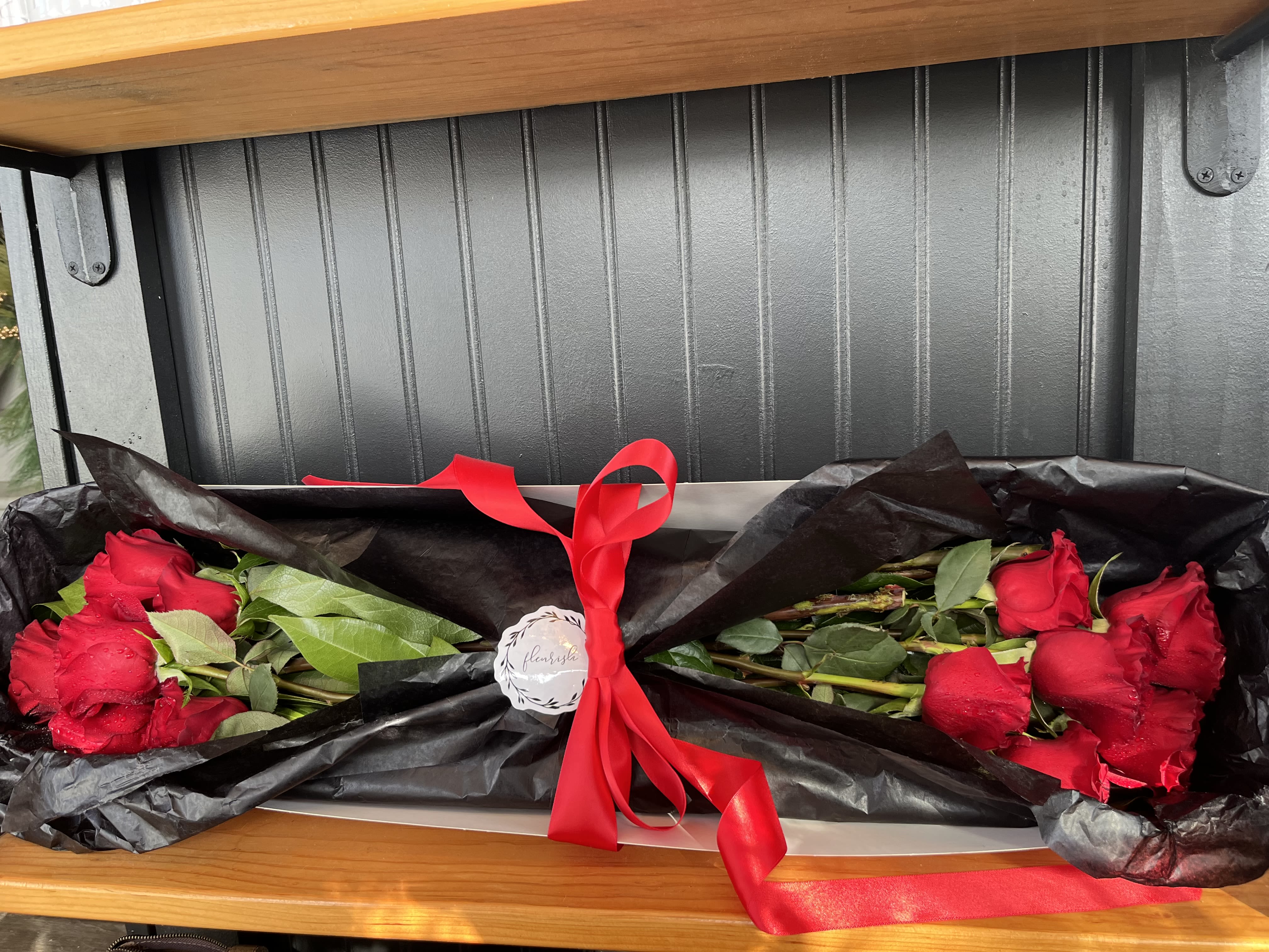Two bouquets of red roses wrapped in black paper with a red ribbon