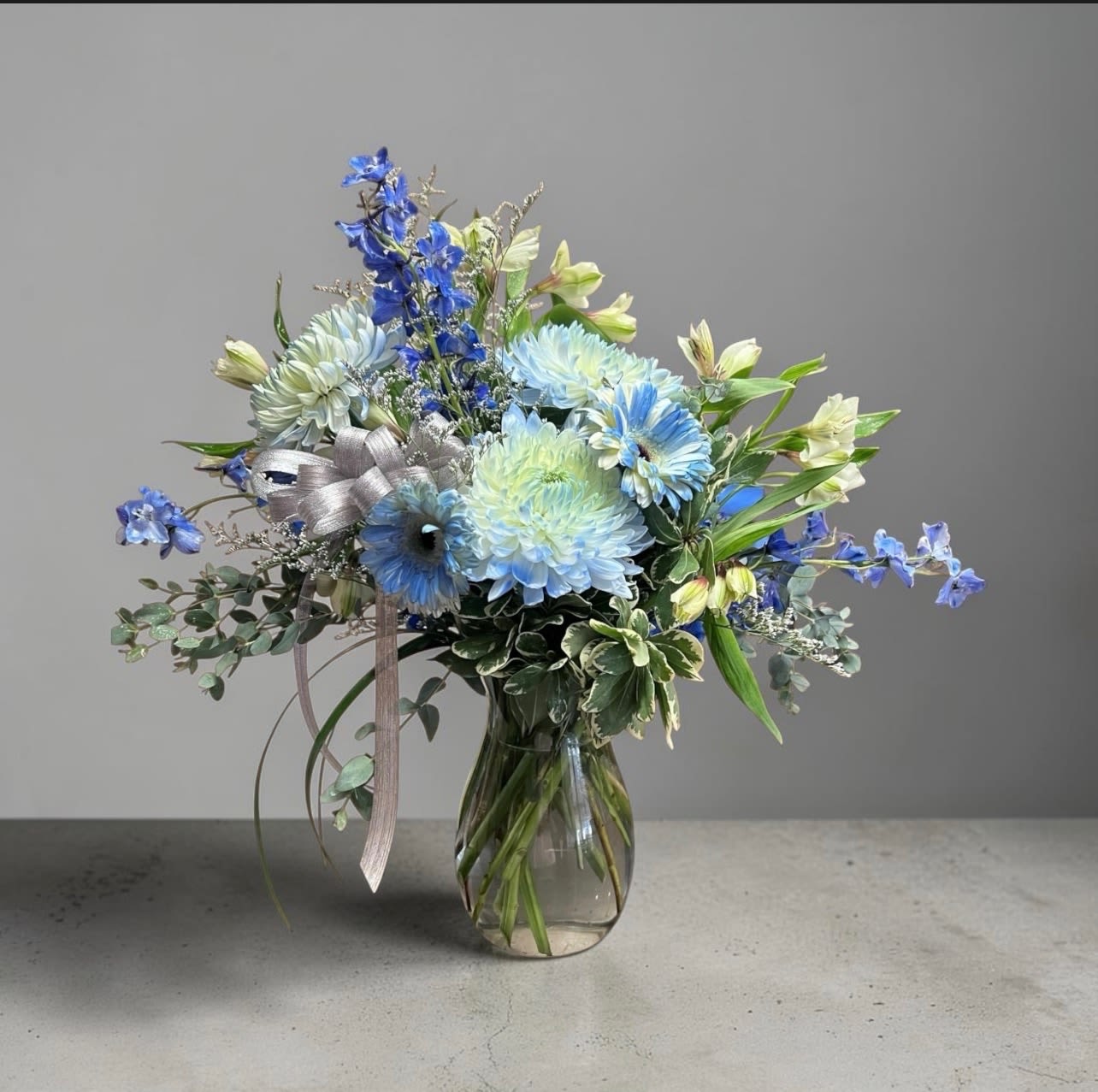 The Brighton - The Brighton is a refined blend of cool blue Gerber daisies, premium chrysanthemum, delicate delphinium, and lush textured greenery. Crisp, balanced, and quietly sophisticated perfect for birthdays, thank you gestures, celebrations or simply sending something beautiful Just Because. 