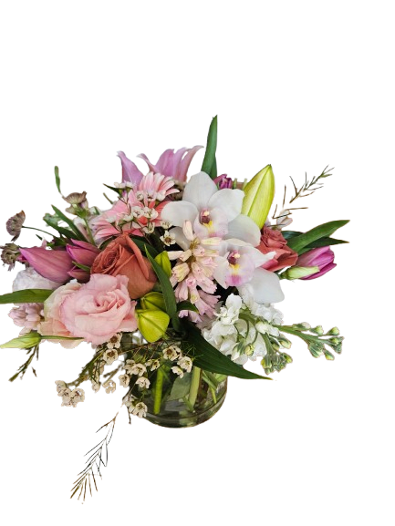 Blush Orchid Garden - A graceful garden-style arrangement featuring elegant white orchids, soft pink roses, fragrant lilies, tulips, and delicate seasonal blooms gathered in a clear glass vase. Designed with romantic blush tones and lush greenery, Blush Orchid Garden brings timeless beauty and sophisticated charm to any celebration or heartfelt moment.