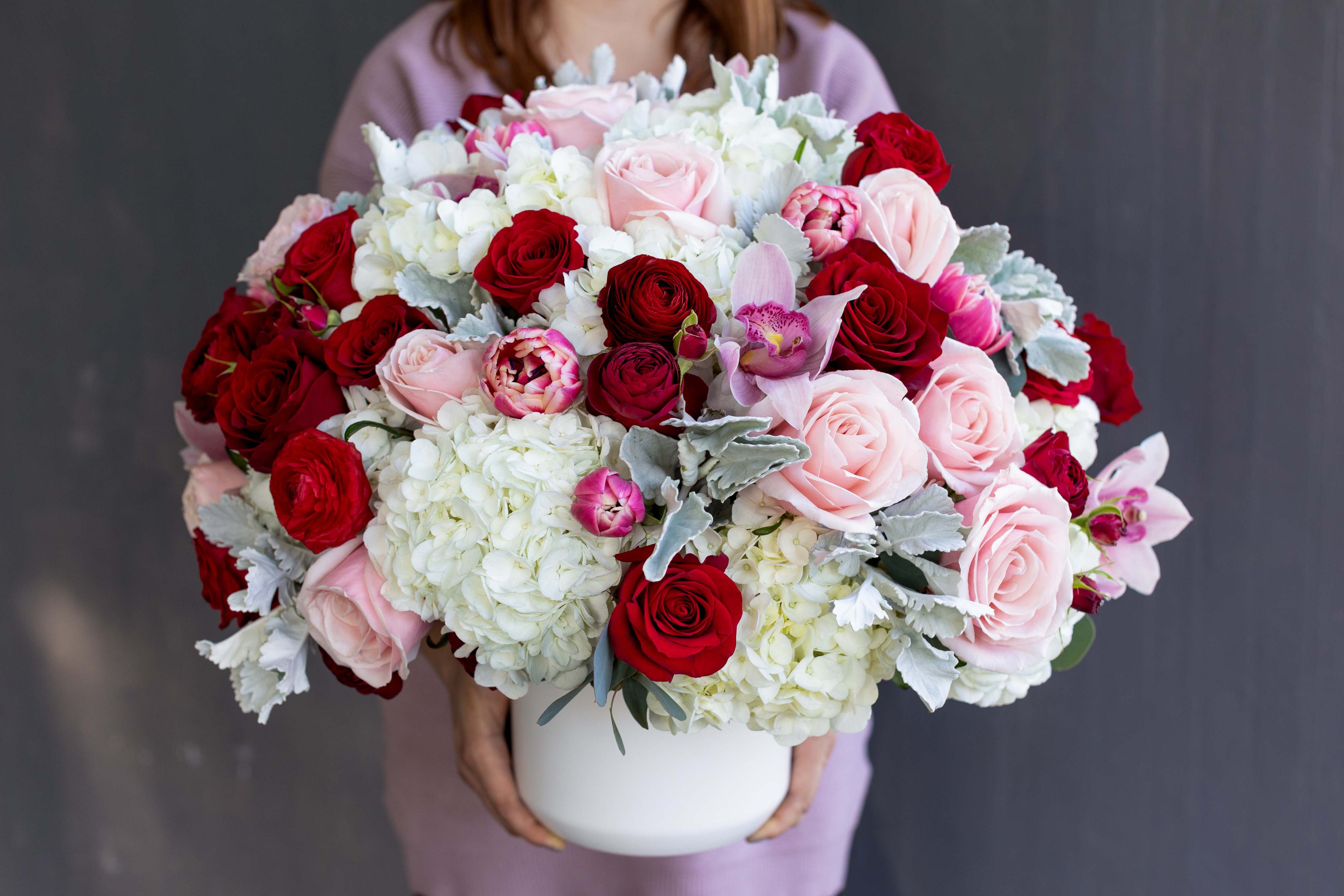 First Love- The Signature Collection - Embrace the feeling of your first love: exciting, beautiful, and full of promise. The hues of pale pink, red, and white blend into the most stunning round arrangement of breathtaking Ecuadorian roses, exotic cymbidium orchids, and soft white hydrangeas. Send your heart in a vase with this beautiful and luxurious arrangement.    This arrangement is offered as part of our Signature Collection. Due to the nature and scale of this design, we cannot offer same day delivery on any of our Signature Collection designs. We want to ensure the finest designs, and take care to ensure each arrangement is crafted with the highest quality flowers. Although we strive to create each arrangement as close to our photos as possible, there is always the chance that some flowers may be seasonally unavailable. In this case, we would substitute with flowers of a similar look and quality, without sacrificing the value of the design. Each arrangement will adhere to the color pallet and look of the arrangement ordered.     SIZE: This flower arrangement is approximately 20” height and 20” width.  FAQ Q: What time will my flowers arrive and what if no-one is there to accept them? A: Excellent question! For full details around our delivery process and timings, please see our Terms and Conditions. Q: May I request to change the design a bit? A: Yes, please make a note in the SPECIAL INSTRUCTION box when you place your online order. We will do our best to follow them.