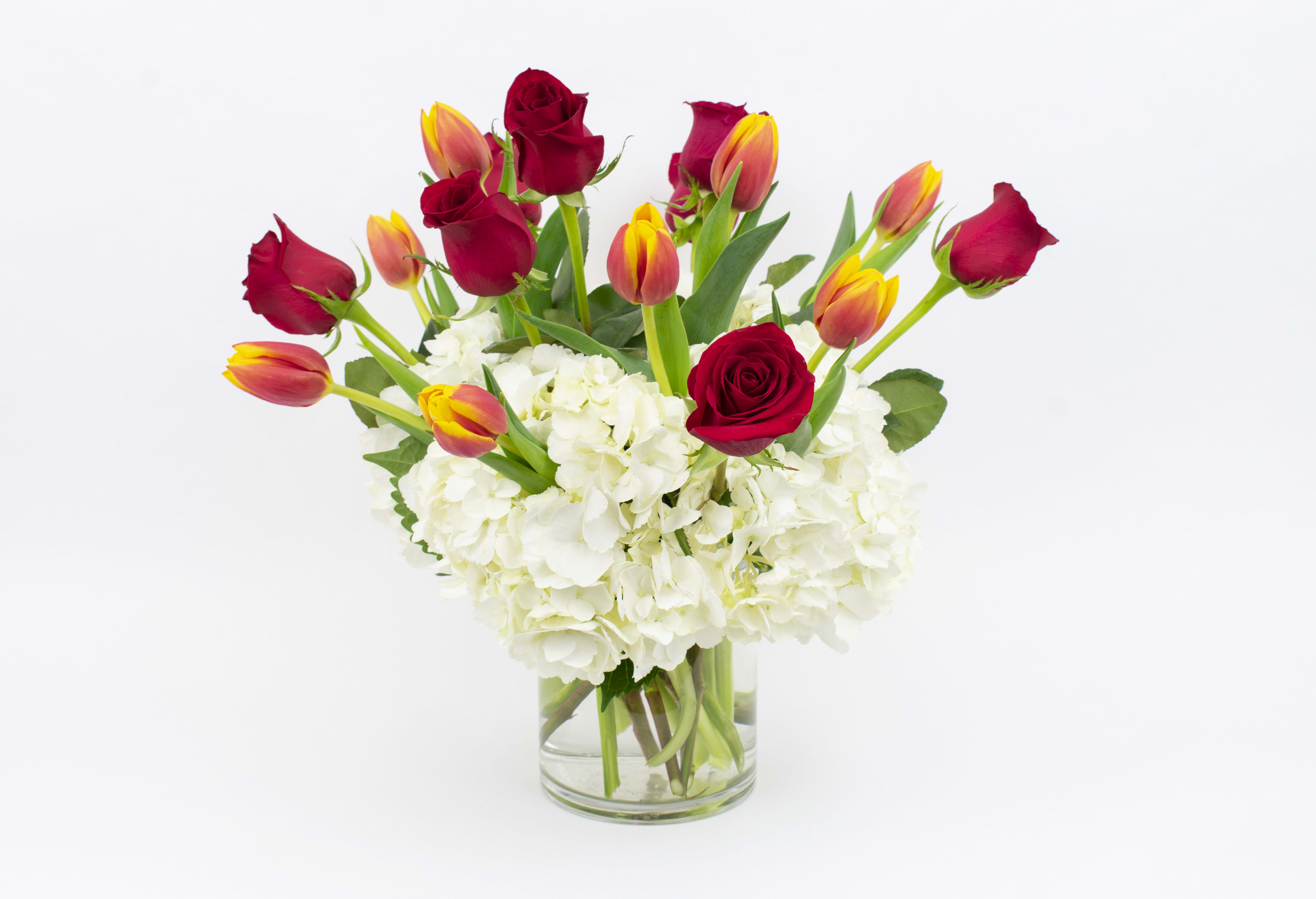 Red roses and orange tulips in a clear glass vase with white hydrangeas