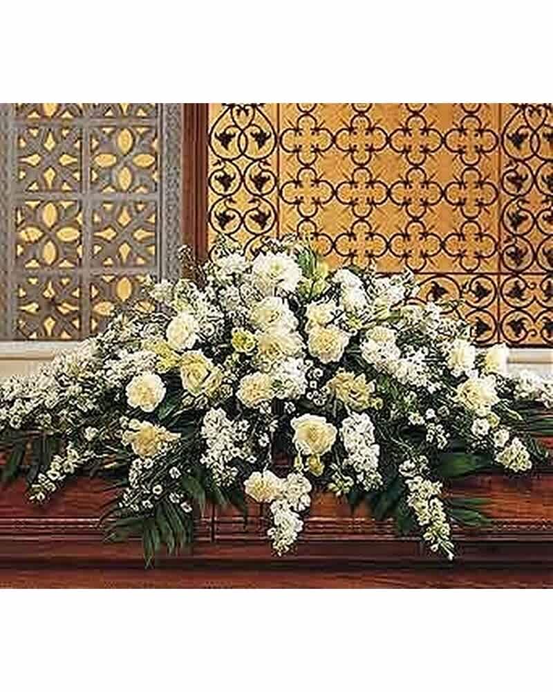 Large white and cream floral casket spray arranged across a wooden casket