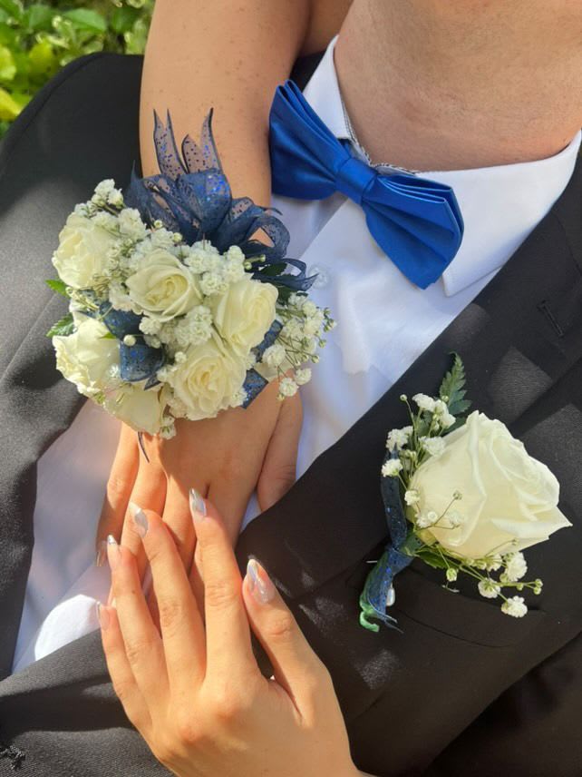 White rose wrist corsage and matching boutonniere with blue ribbon on a couple in formalwear