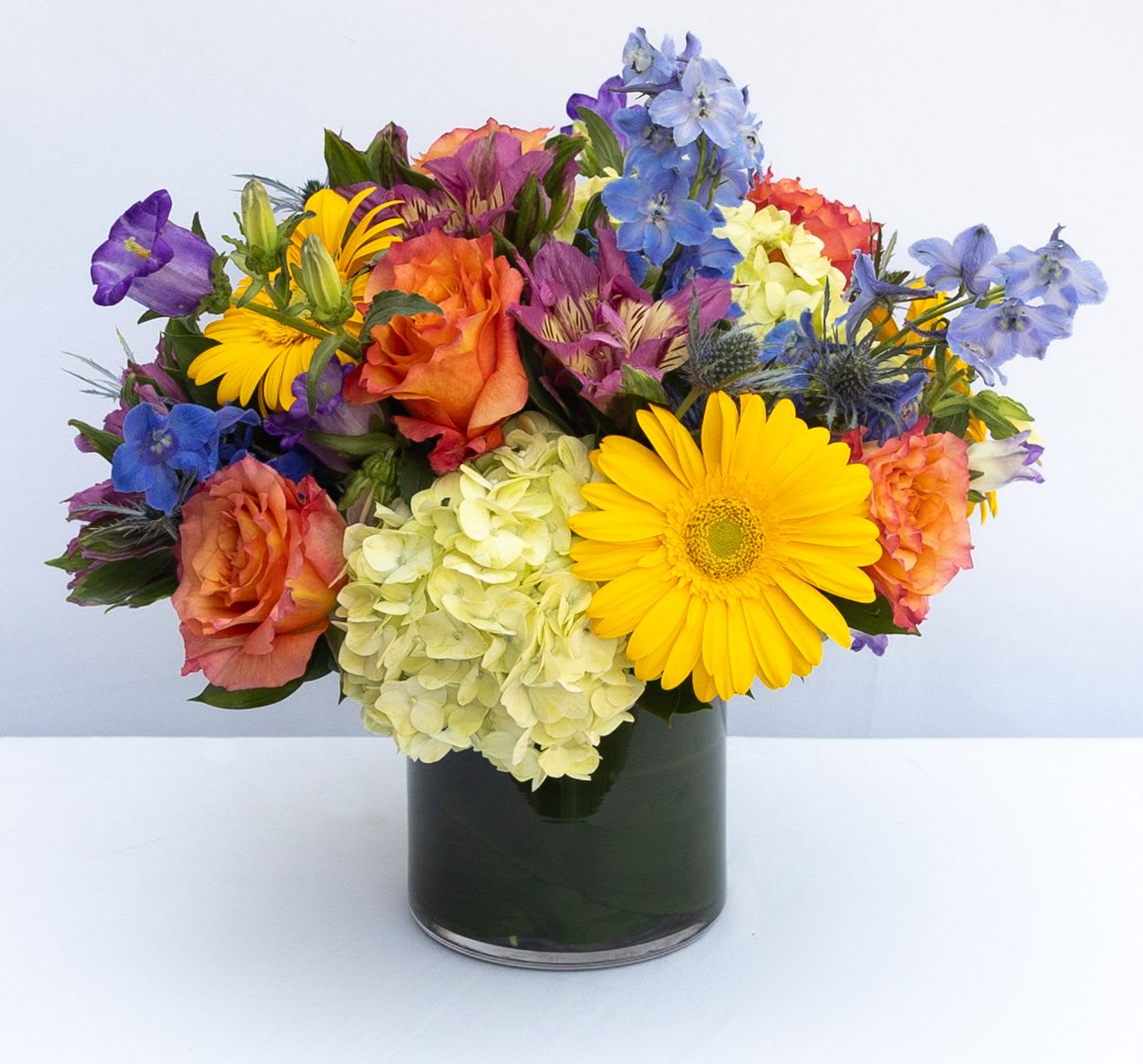 Mixed bouquet of roses, hydrangea, and daisies in a dark glass vase