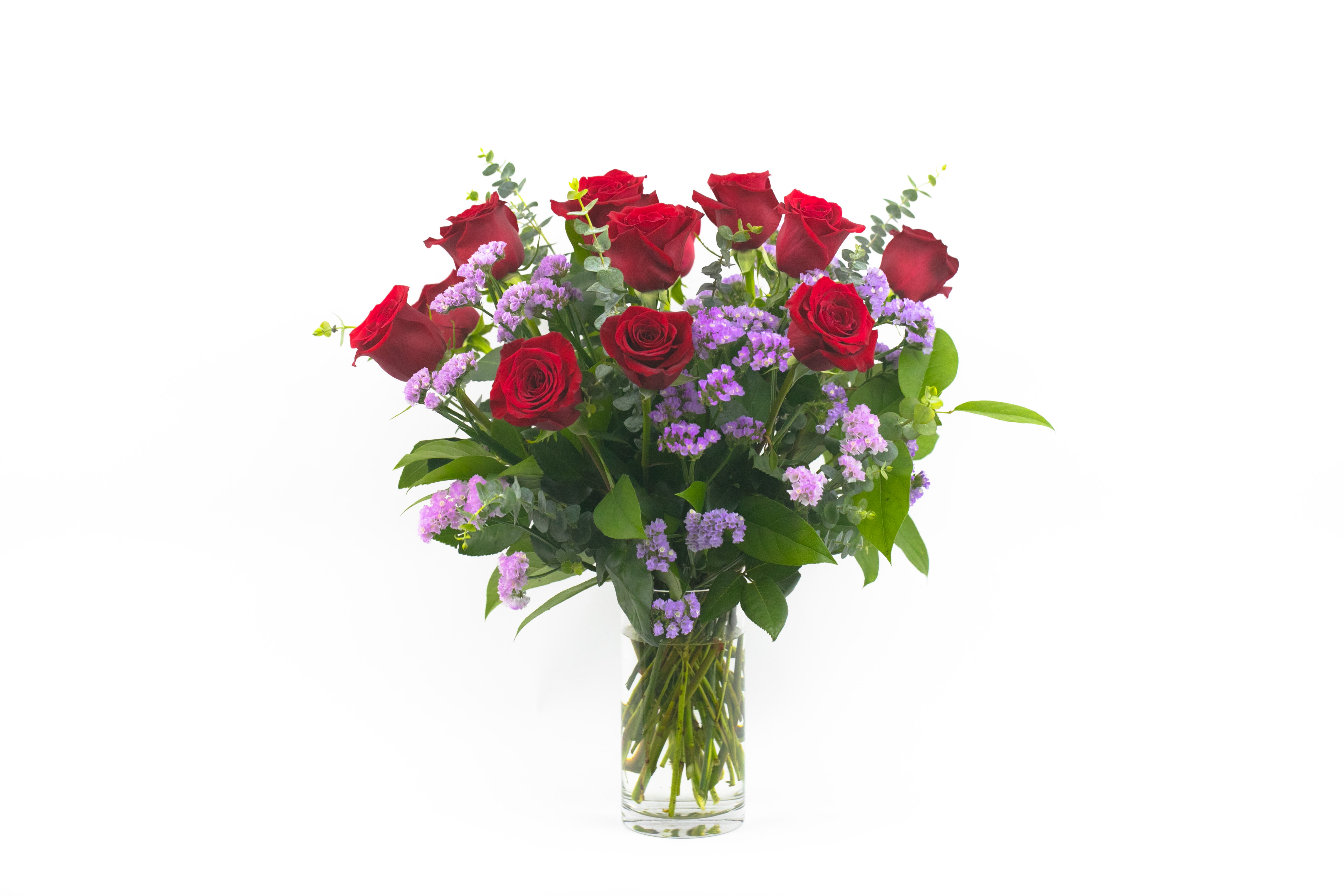 Red roses and purple filler flowers in a clear glass vase