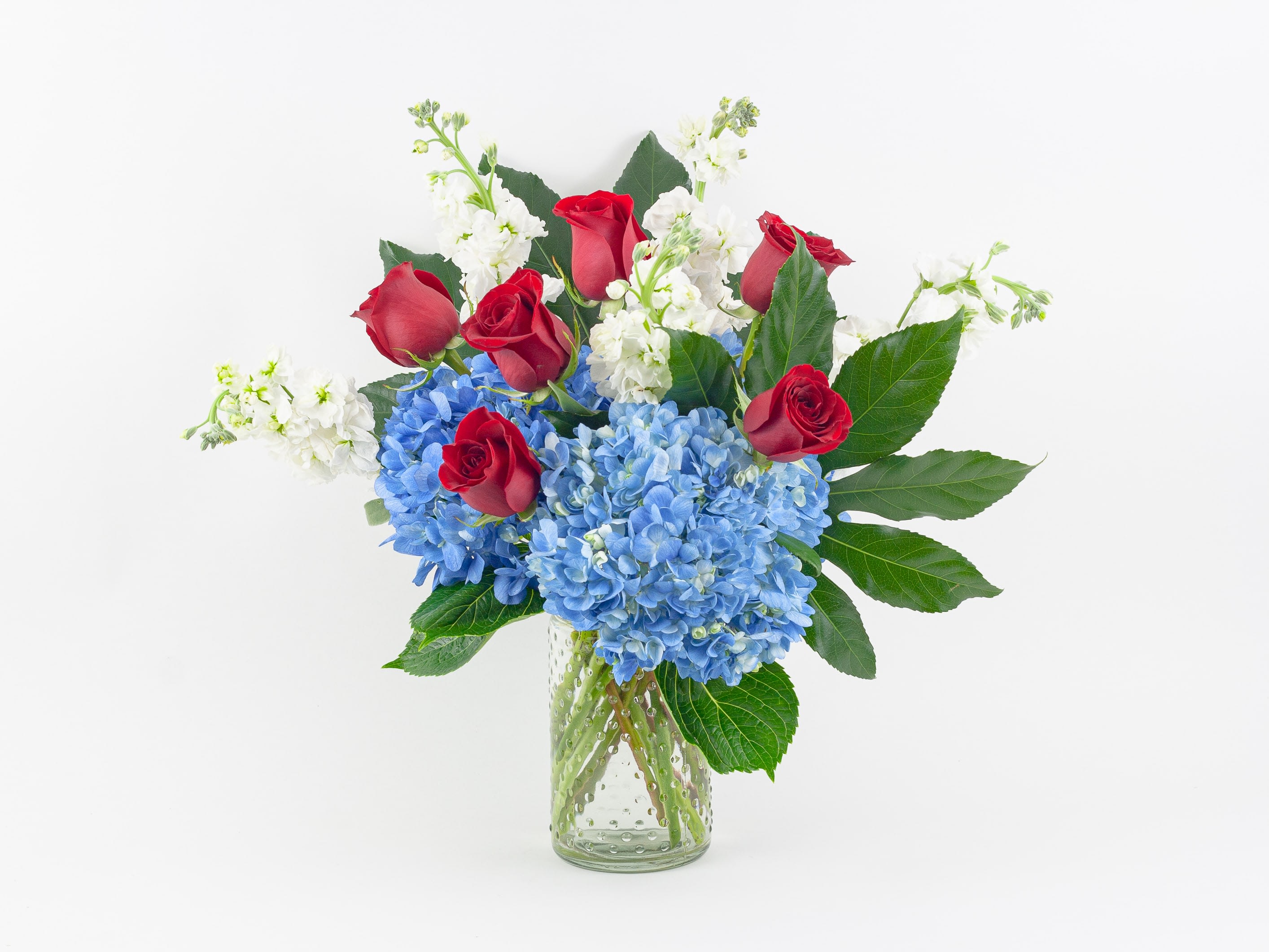 Red roses and blue hydrangeas in a clear glass vase