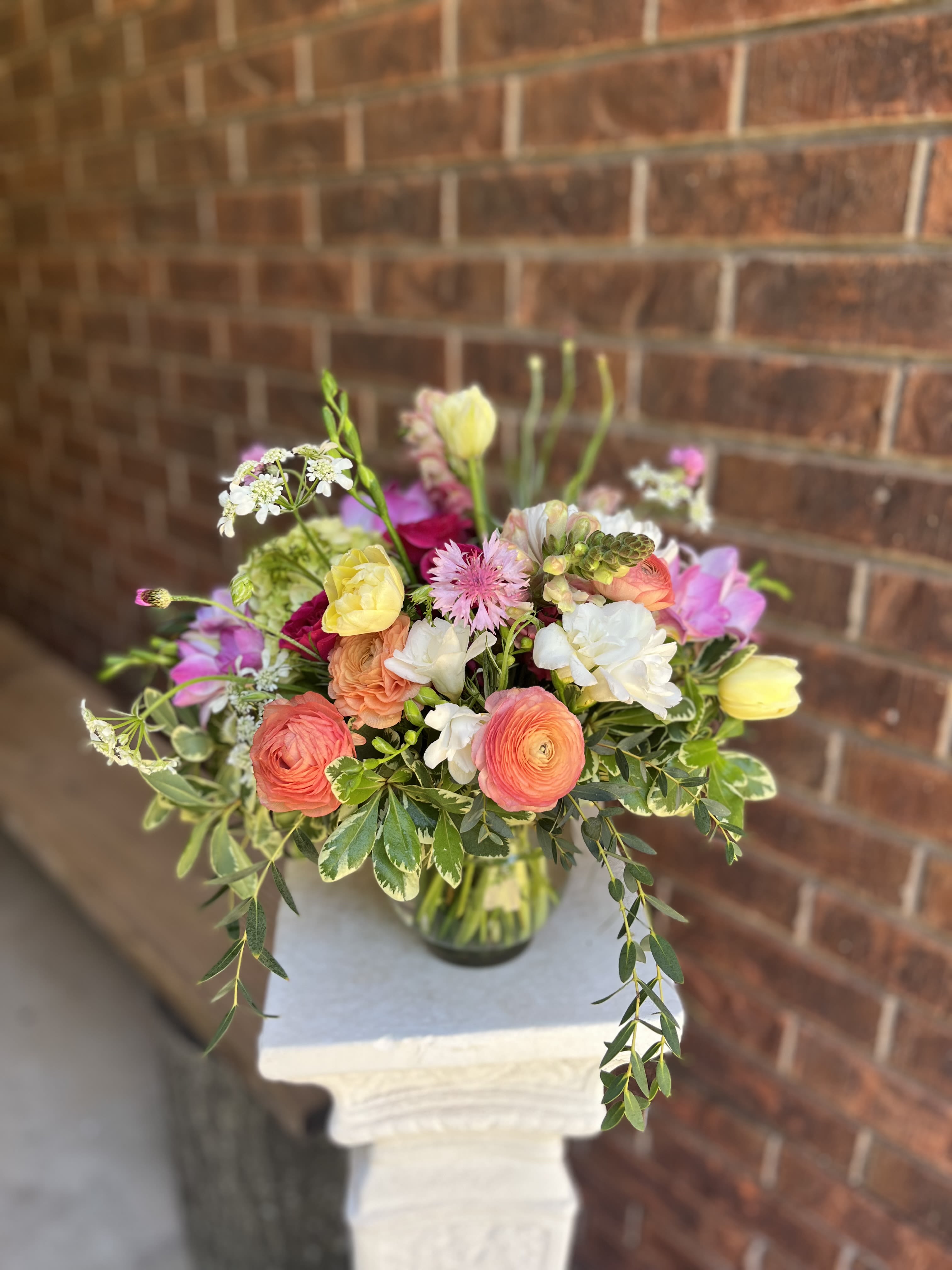 Thinking of you - A lavender hydrangea crown paired with peach and pink tulip buds makes this spring bouquet feel like a fresh-picked moment - perfect as a birthday bouquet or a cheerful arrangement to celebrate someone special. The combination of pastel lavenders, peach, pinks and touches of deeper coral reads romantic and whimsical, so the person you're thinking of will feel genuinely seen and celebrated.  The bouquet mixes hydrangeas, tulips, ruffled carnation-style blooms, ranunculus and freesia with fine airy filler stems and trailing greenery for a loose, garden-style silhouette. Options include a soft white wrapping tied with a pink ribbon and an optional clear glass vase; colors run from pale white and peach through pink, purple, yellow and orange, giving both soft and saturated accents. Sizes and final stem counts vary by order; a gift card can be added to personalize your message.  Ideal for spring gifting, birthdays, or any everyday celebration where you want to brighten someone's day - this arrangement arrives ready to display in the included vase or wrapped for hand delivery. To keep blooms fresh, place in clean water, trim stems at an angle, and refresh the water every couple of days.