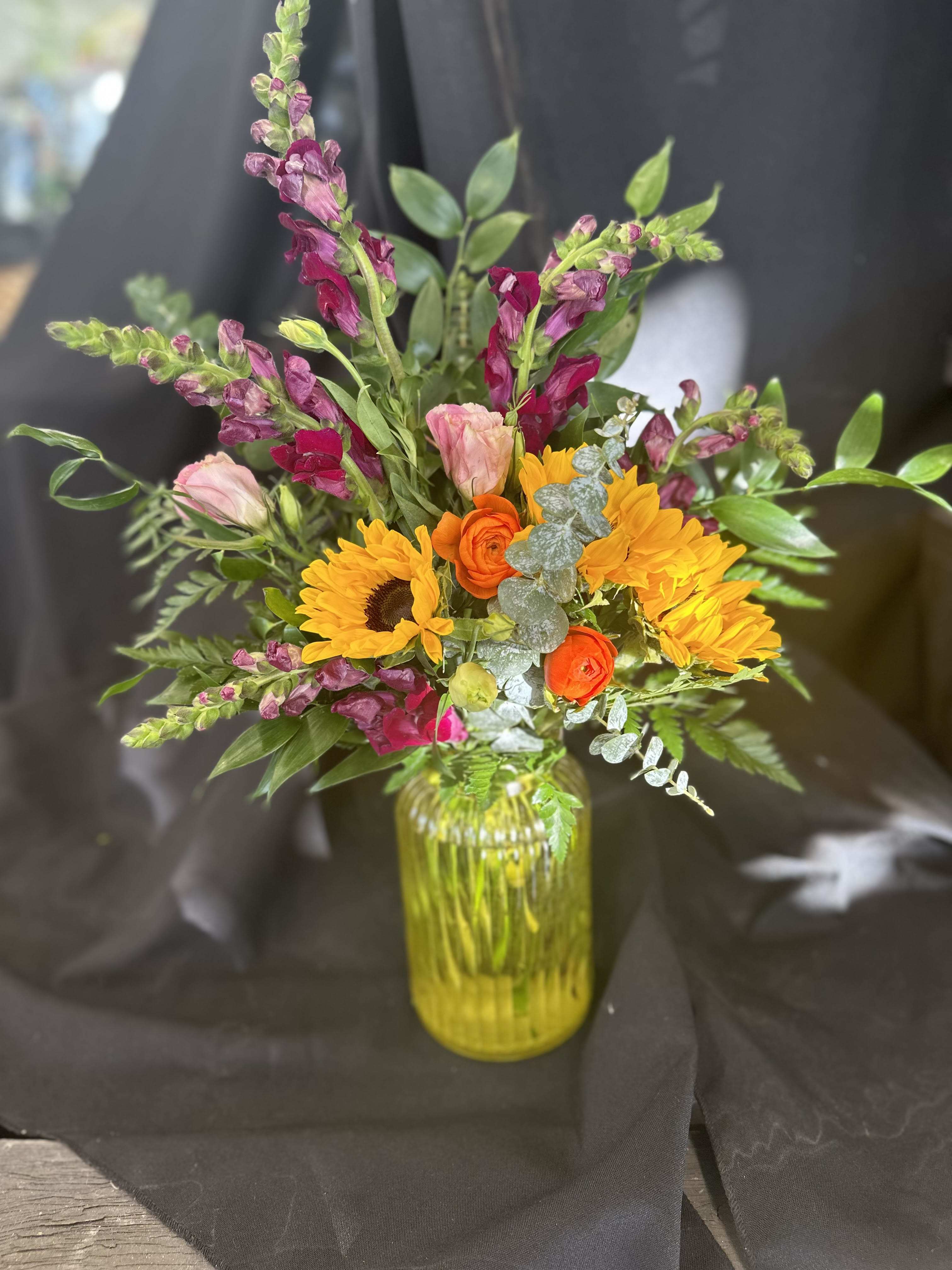 Sunshine - Designed using pinky burgundy snapdragons, sunflowers, pink lisianthus, queen anne's lace, and orange ranunculus, with spiral eucalyptus, and italian ruscus.