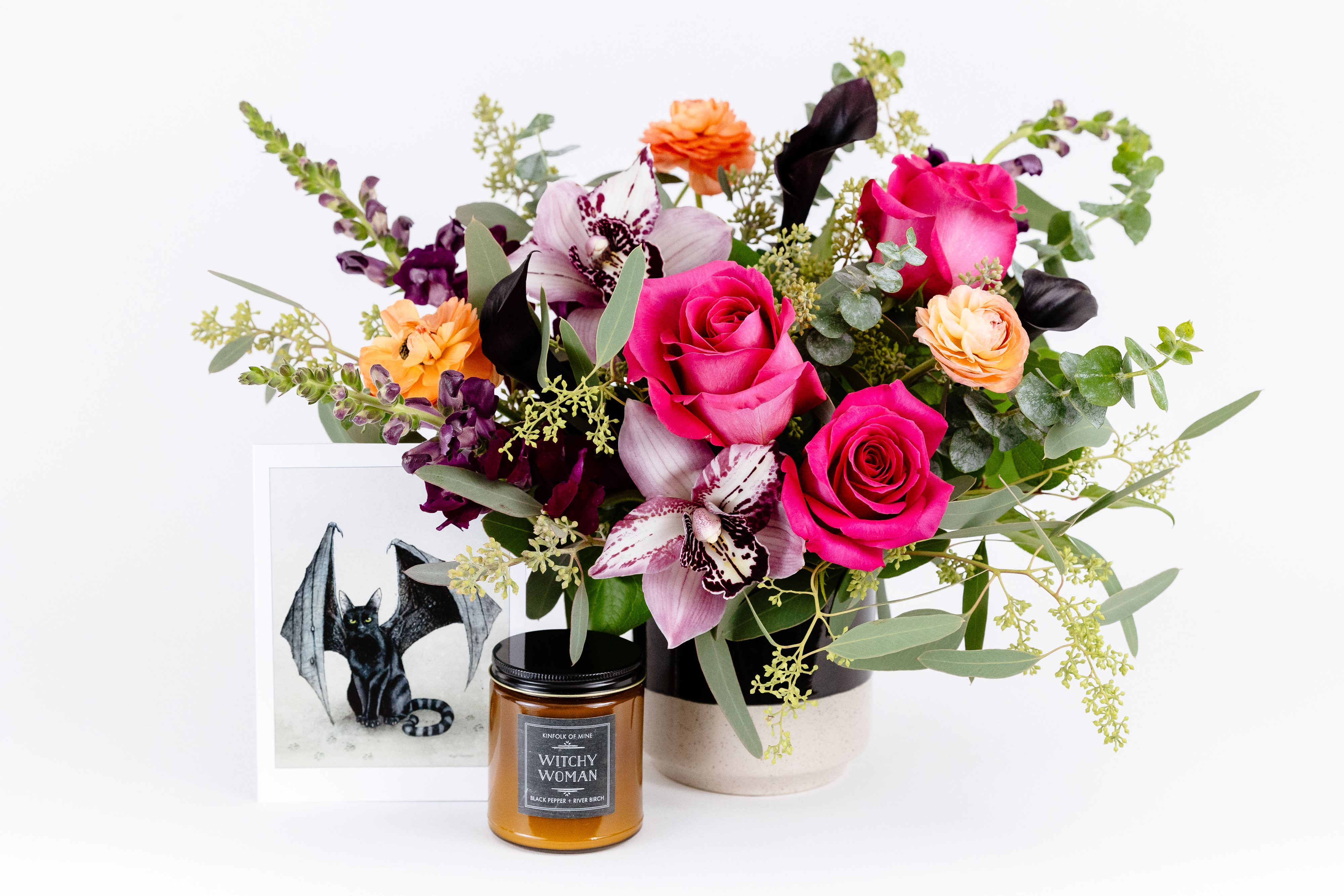 Mixed bouquet with pink roses and orchids in a vase beside a candle and framed bat print