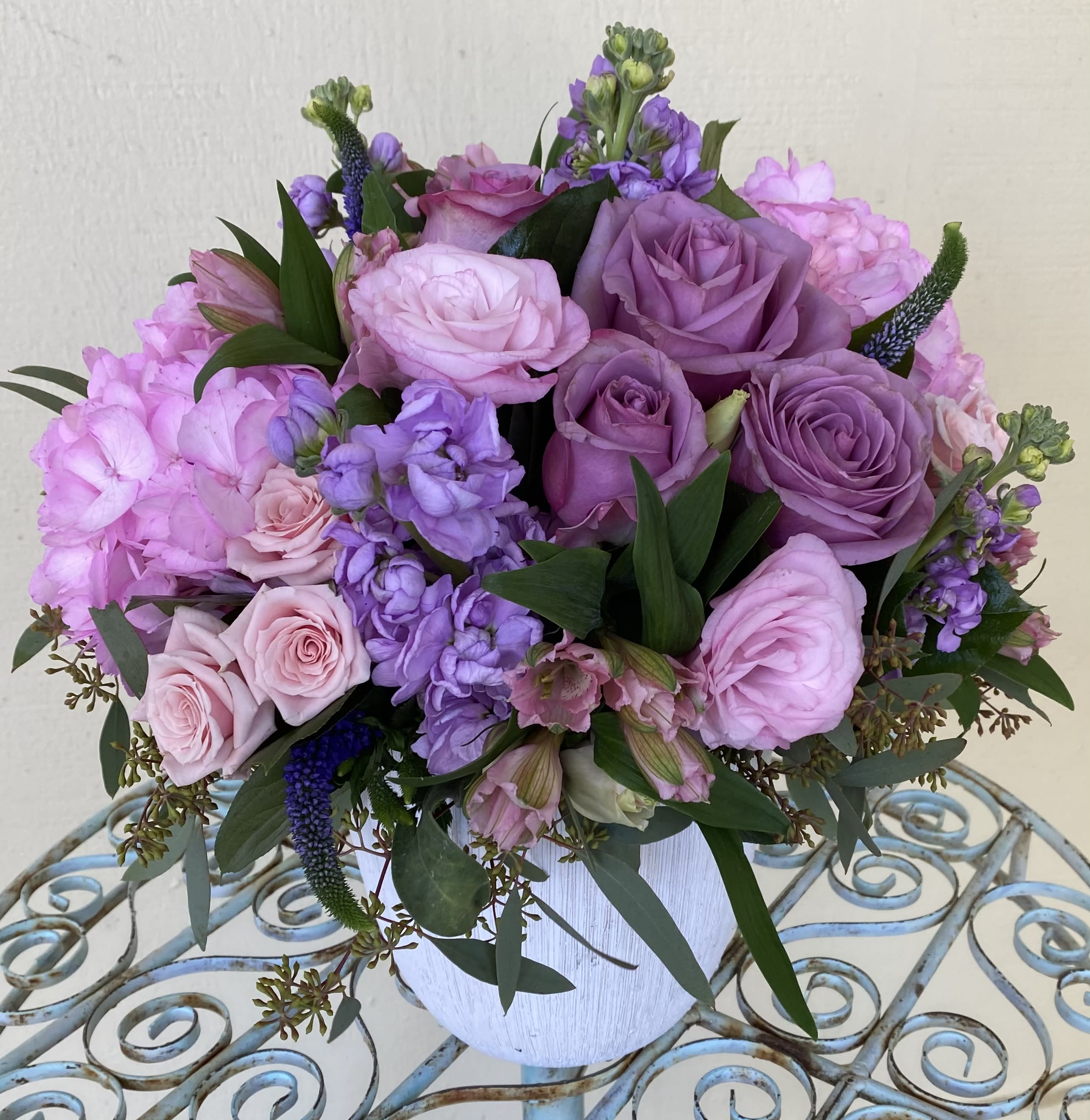 Round arrangement of pink and lavender roses with mixed blooms in a white vase.
