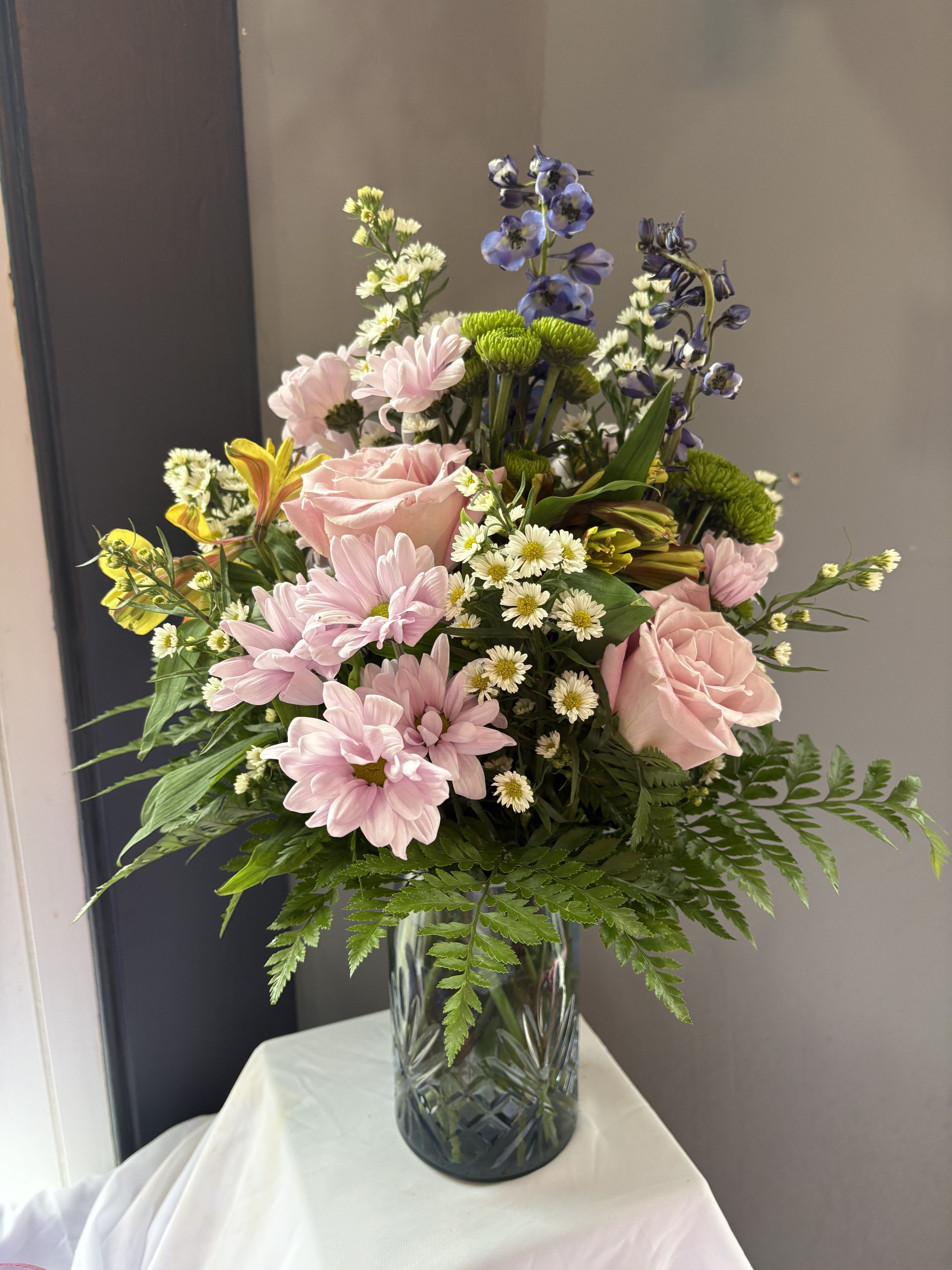 Frazier's Version Blue Belle Bouquet - Frazier's Version Blue Belle Bouquet is a sweet Mother's Day flower arrangement of soft pink, lavender, blue, yellow, green, &amp; white blooms, beautifully presented in Teleflora's Blue Belle Vase keepsake-perfect for celebrating Mom with fresh spring charm. The scale of the arrangement should determine the type of substitution acceptable, but the substitution must be of equal or greater value and must maintain the style and color harmony of the original order.