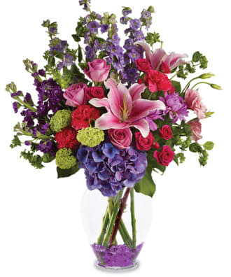 Mixed bouquet of pink roses, lilies, and purple flowers in a glass vase