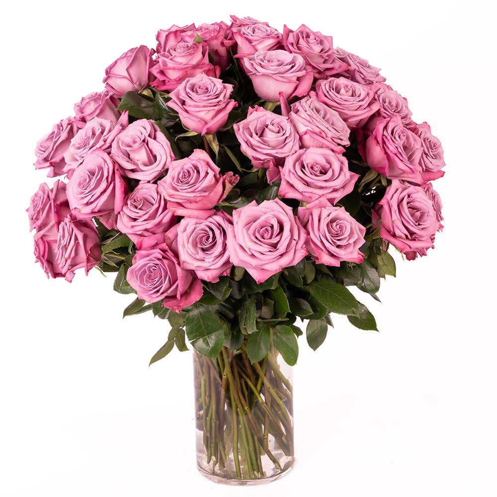 Large bouquet of pink and lavender roses arranged in a clear glass cylinder vase