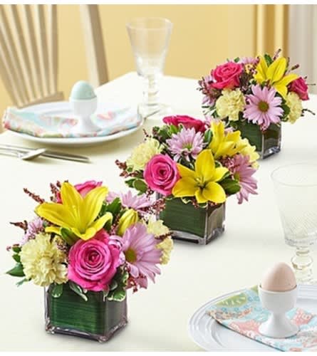 Three small floral centerpieces in square glass vases on a table