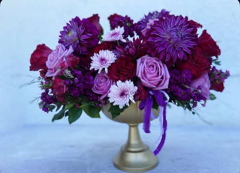 Purple and pink flower arrangement in a gold pedestal vase