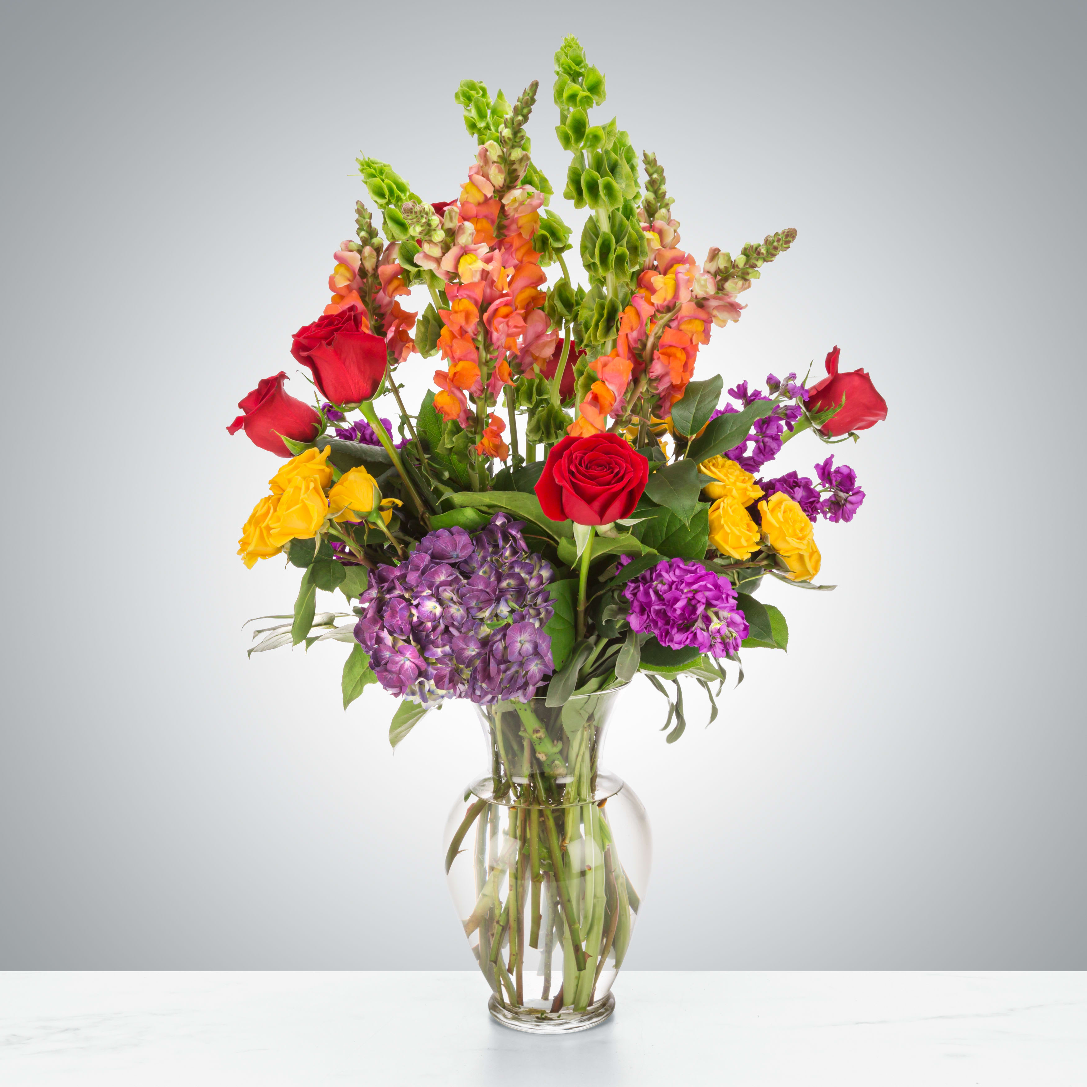 Mixed bouquet of roses, hydrangeas, and snapdragons in a clear glass vase