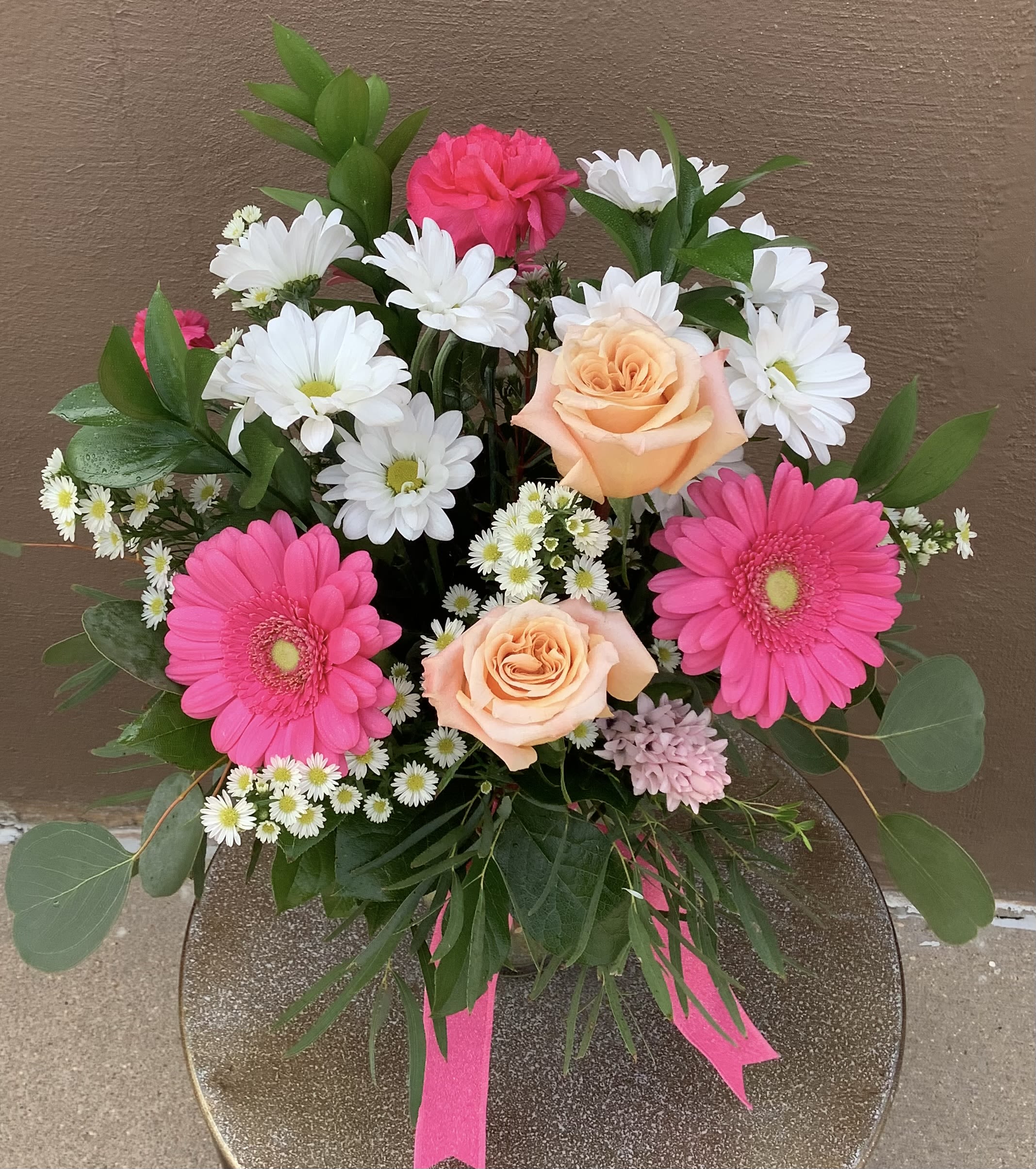 My Sweet Momma - Bright pink gerbera daisies take center stage in this cheerful flower arrangement, paired with soft peach roses and clusters of small white daisy-like blooms for a fresh, spring-ready look-perfect as a birthday bouquet, a thank-you gift, or a "thinking of you" surprise for Mom. The lively color mix of pink, peach, white and green reads joyful and affectionate, the kind of bouquet that makes the person you're thinking of feel genuinely celebrated and seen. 