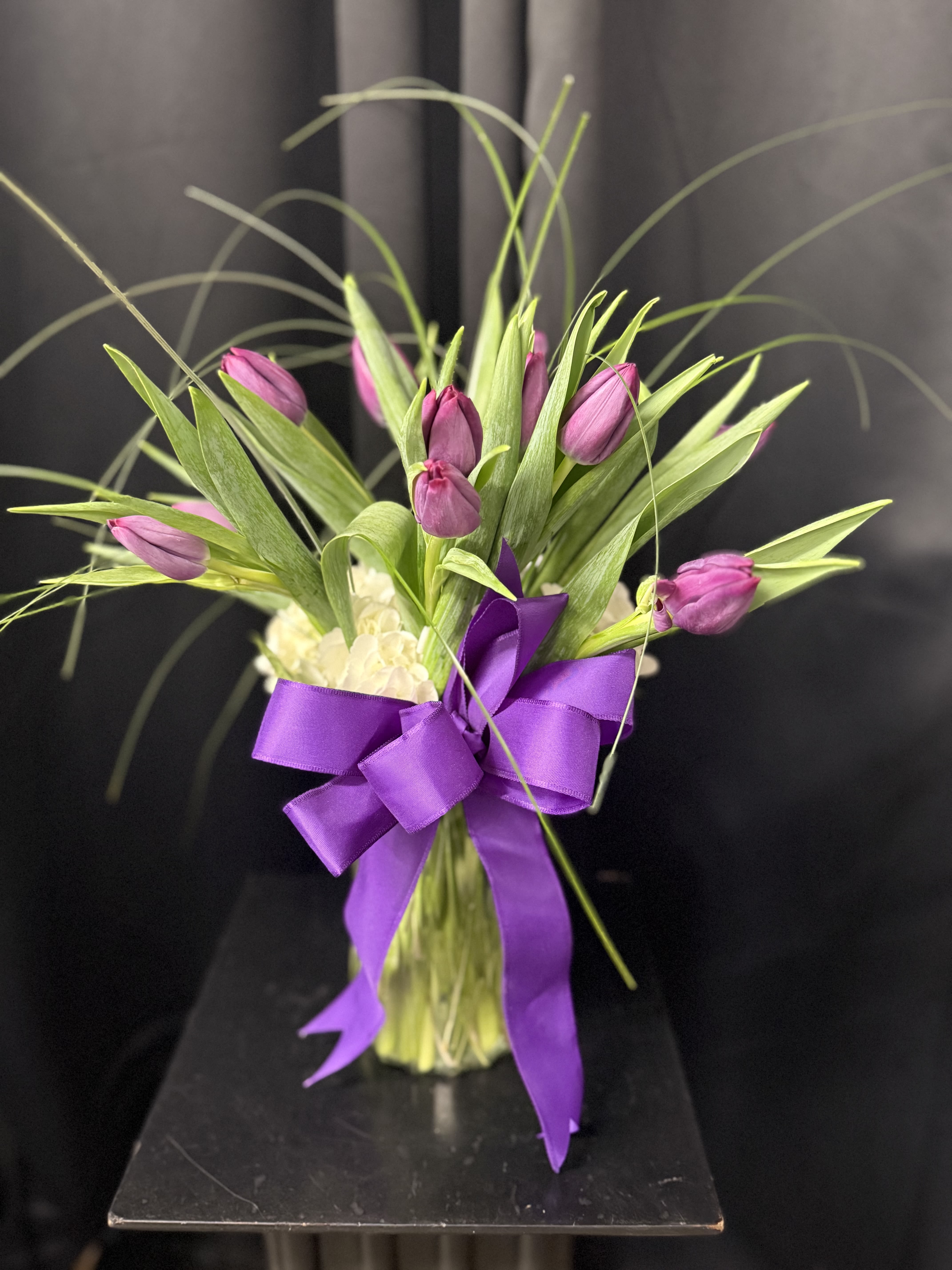 Purple tulips arranged with a large purple ribbon in a clear vase