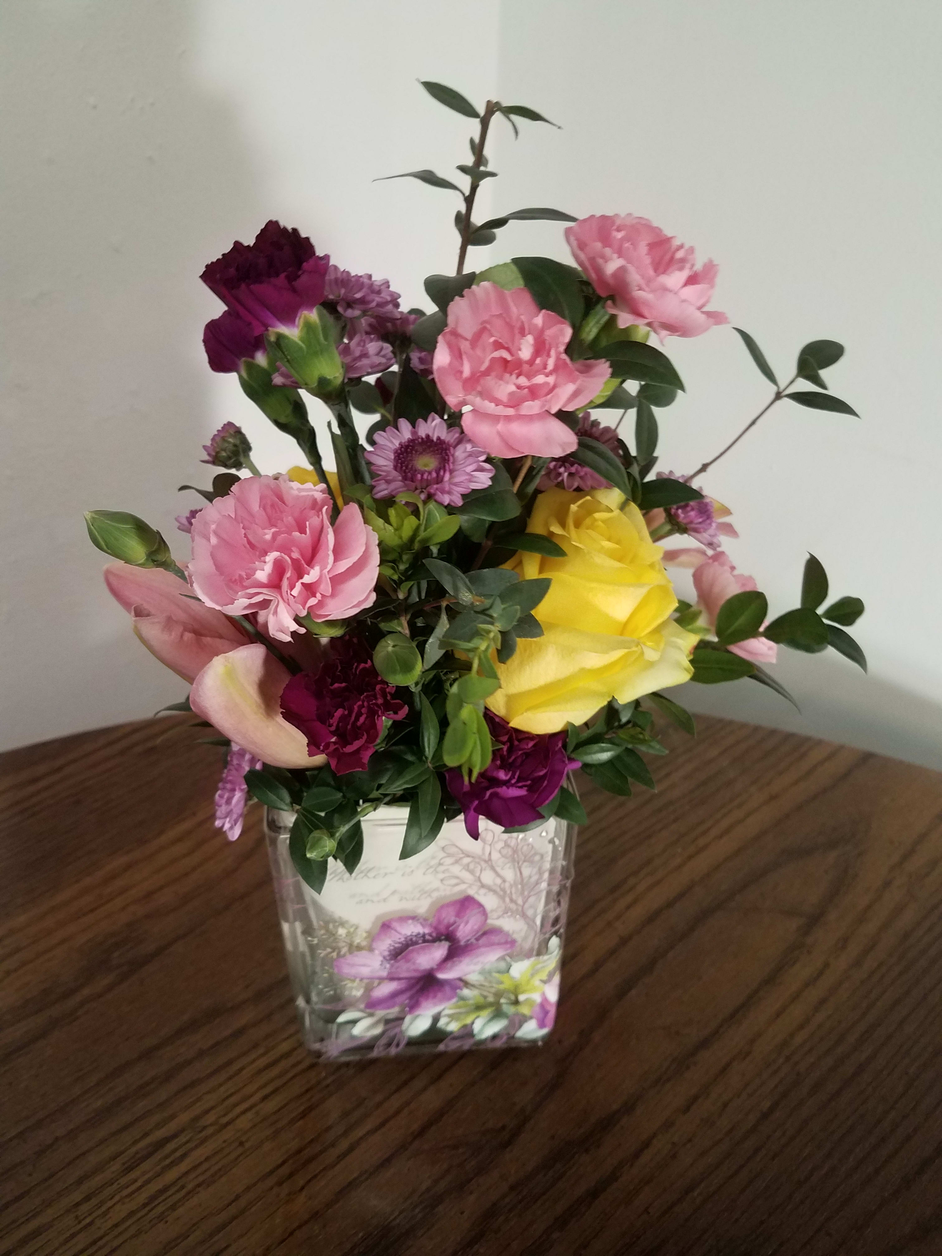 Mixed pink, purple, and yellow flowers in a clear square vase