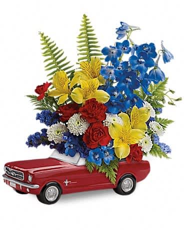 Flower arrangement in a red toy car with blue, yellow, red, and white blooms