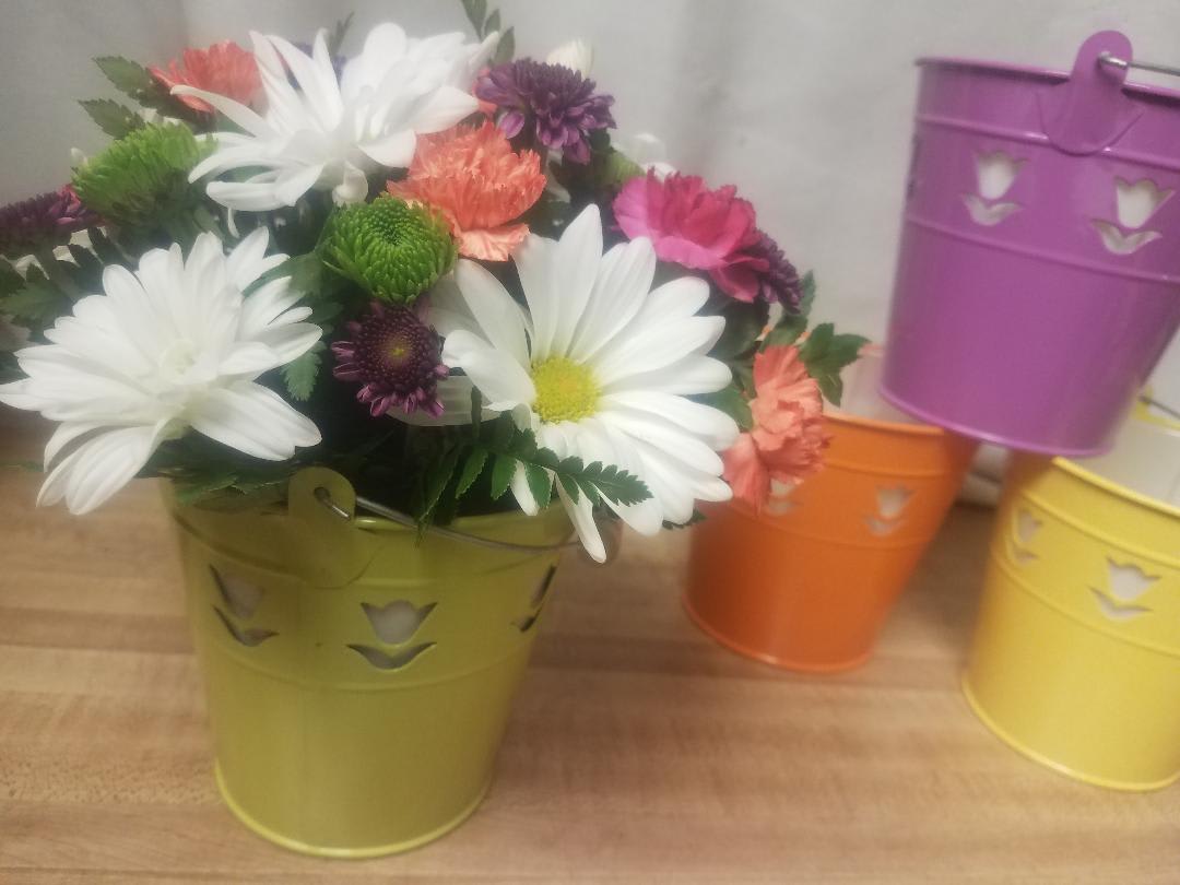 Mixed daisy bouquet in a green metal bucket with colorful buckets behind it