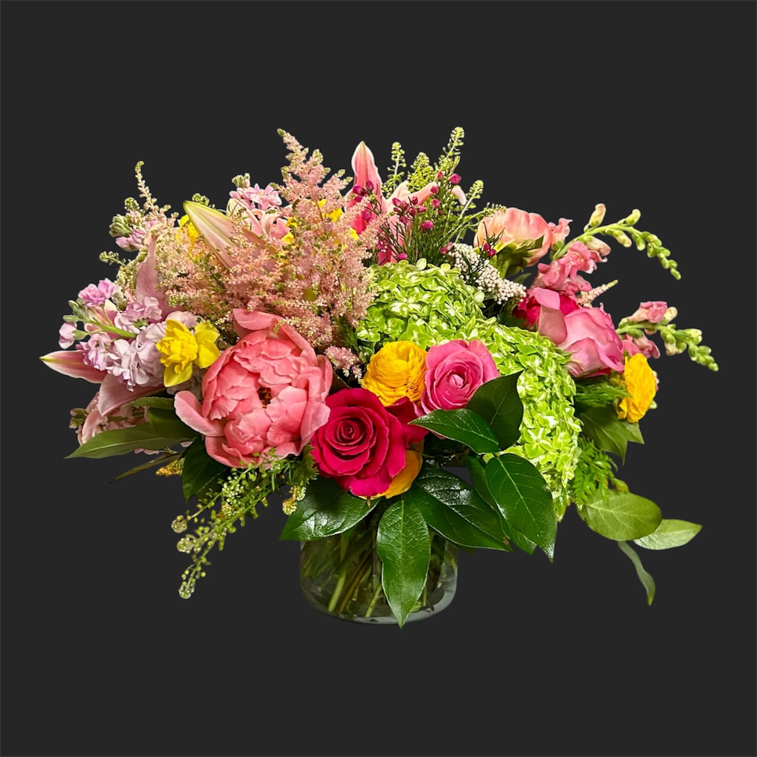 Love Always  - A lush, garden-style bouquet that reads joyful and abundant-perfect as a birthday bouquet, a congratulations arrangement, or a cheerful spring gift for someone special. Bright green hydrangea heads anchor the center while pink and white roses, blousy peonies, and satin lilies unfurl around them, creating a wide, full silhouette that makes the recipient feel truly celebrated.  Textured snapdragons, stock, ranunculus, and smaller filler blooms weave through the composition for airy height and delicate contrast, giving the arrangement a lively, layered look from every angle. Presented in a clear glass vase, this large mixed bouquet balances rounded focal flowers with vertical accents for a polished yet effortlessly garden-fresh impression.