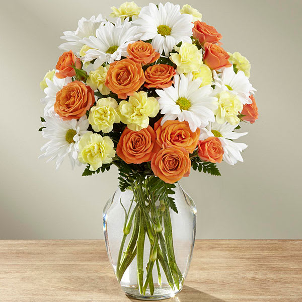 Bouquet of orange roses, white daisies, and pale yellow carnations in a glass vase