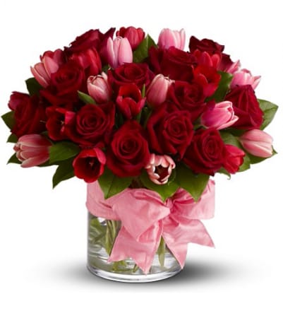 Red roses and pink tulips in a glass vase with a pink ribbon