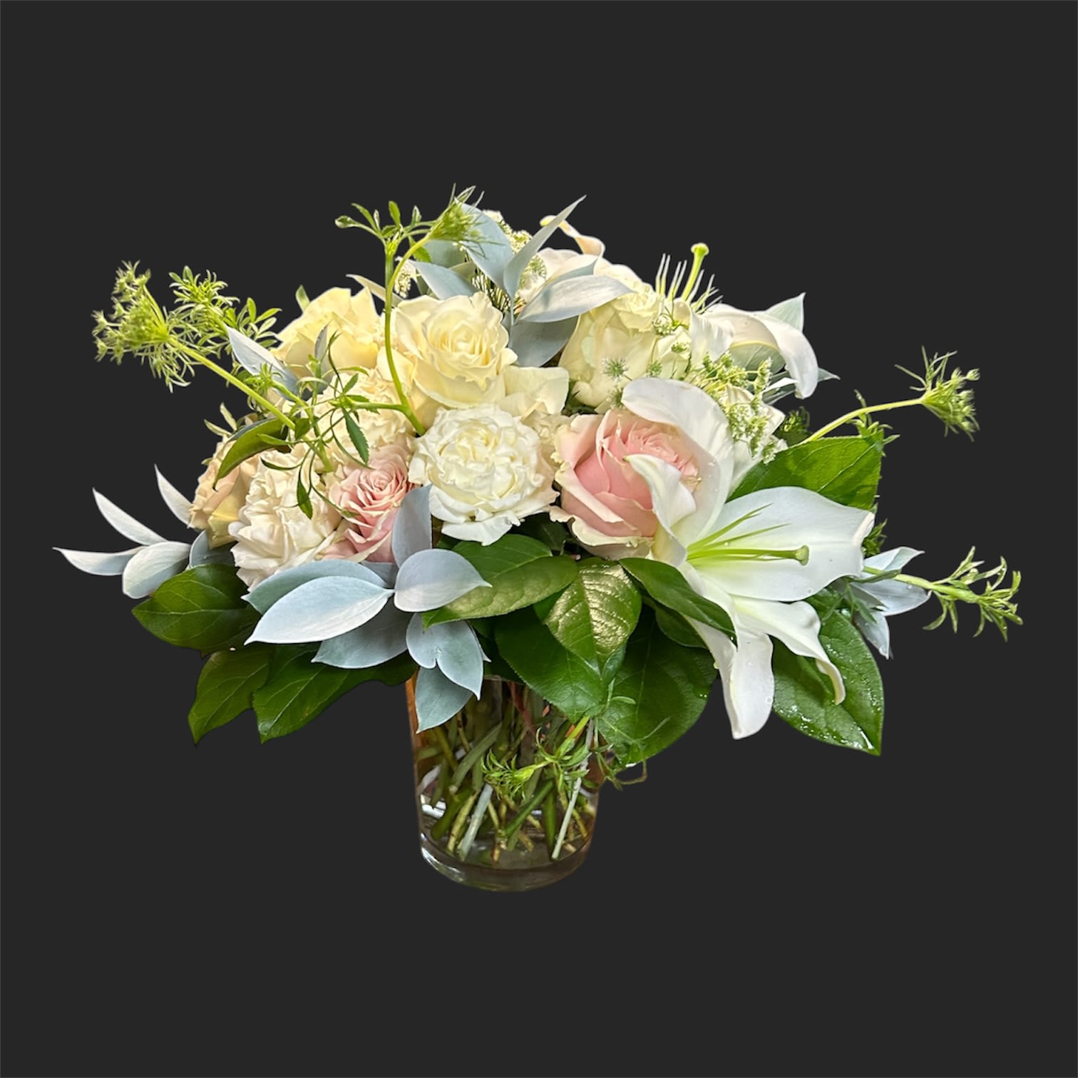 Endless Love  - A compact cluster of white and blush roses with white lilies creates a refined, romantic flower arrangement perfect as a wedding bouquet centerpiece, anniversary gift, or sympathy arrangement. Pale blue-gray foliage and glossy green leaves lend a cool, elegant contrast that keeps the palette soft and serene-an arrangement designed to make the person you're thinking of feel quietly celebrated and comforted.