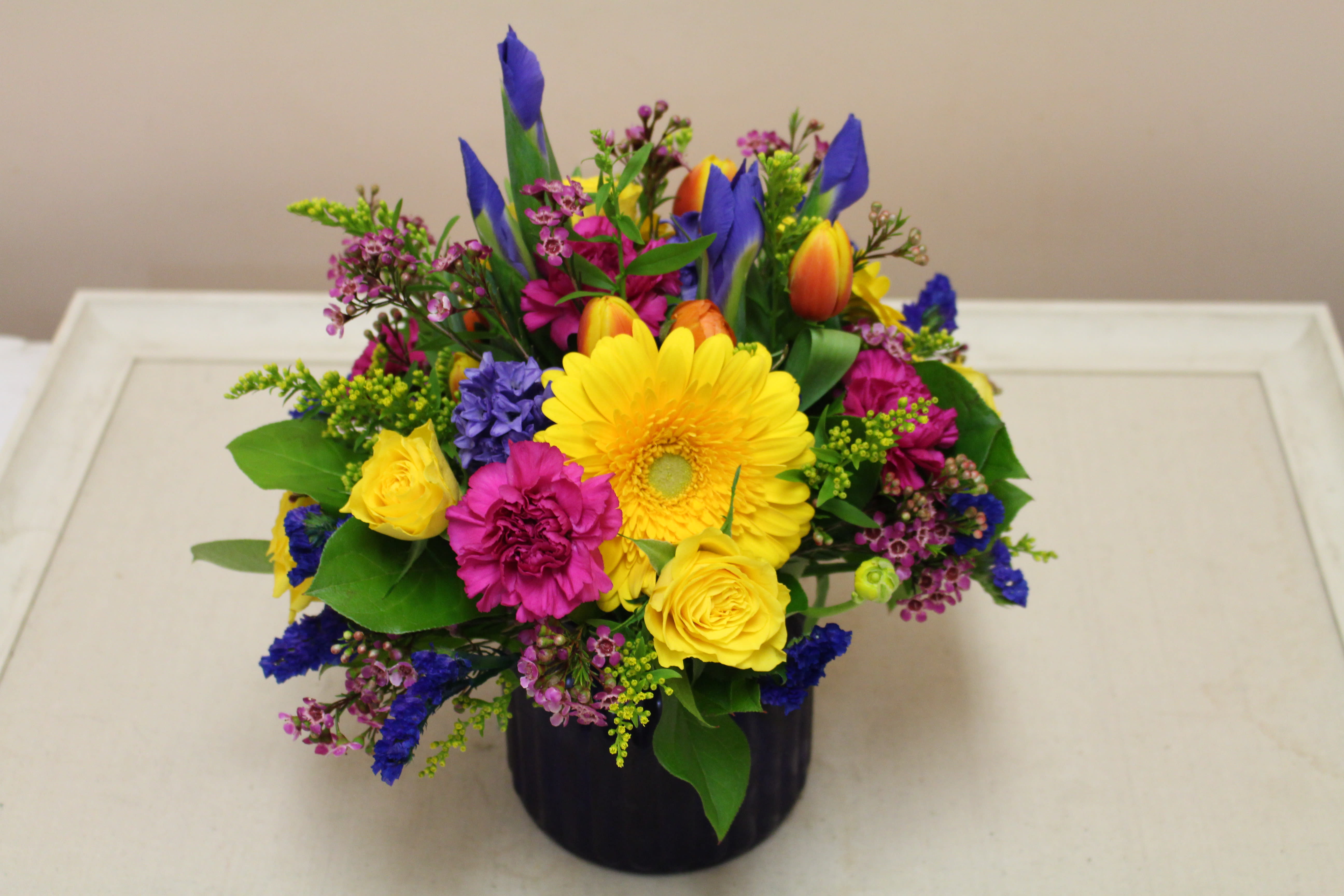 Bright mixed bouquet in a black vase with yellow, pink, and blue flowers