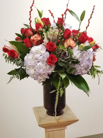 Red roses and pale hydrangeas arranged in a dark vase
