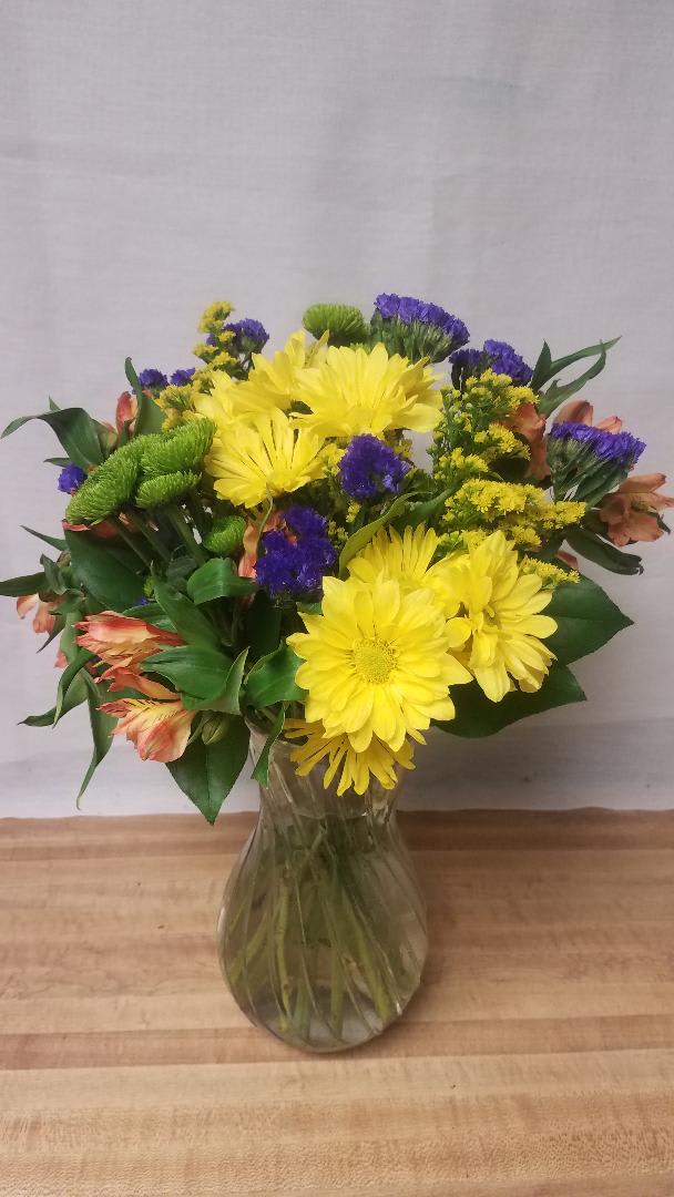 LONG-LASTING  SUNSHINE - Send them some sunshine with this arrangement of yellow daisies, alstromeria, button mums, and purple statice.