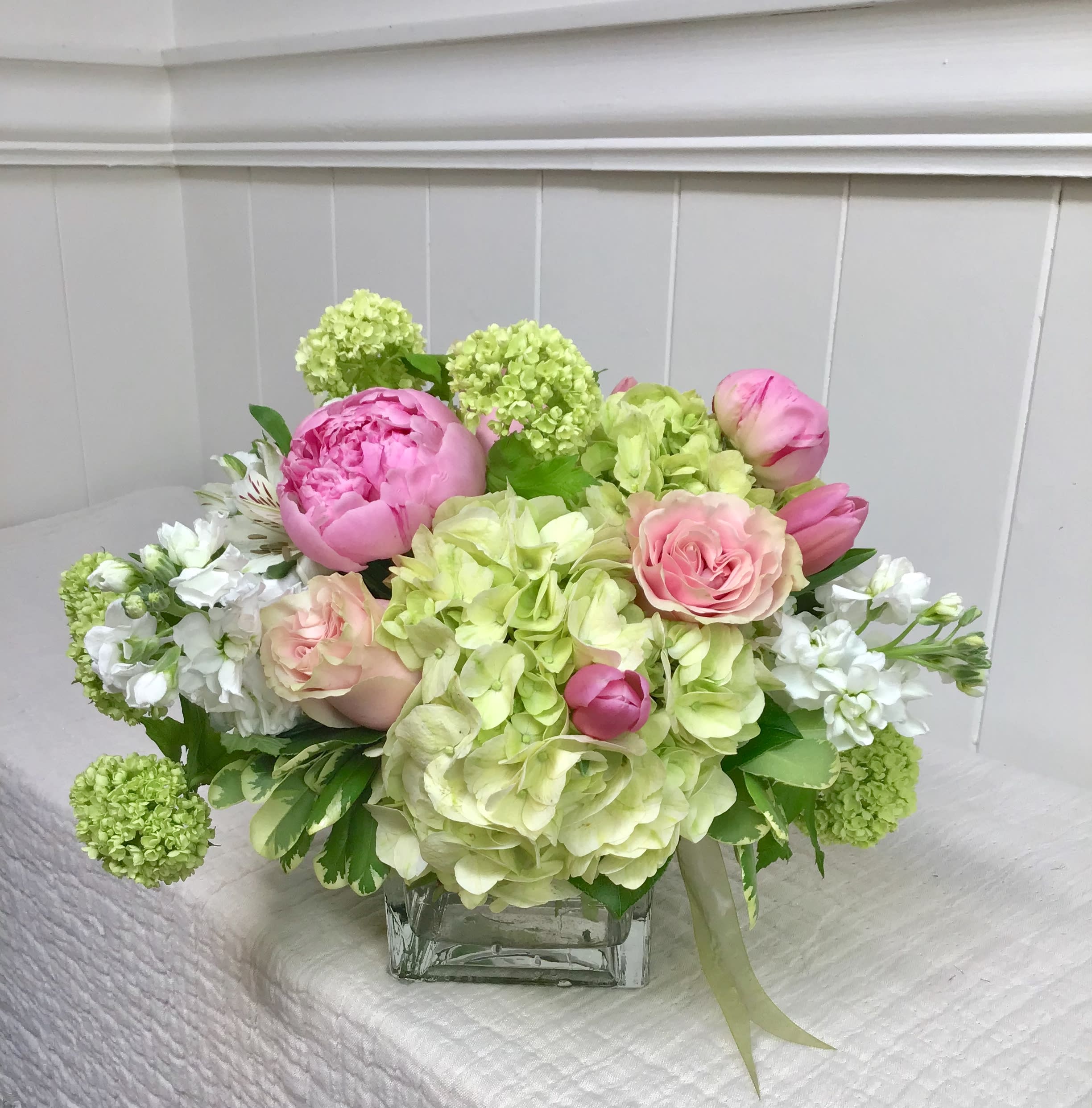 Pink peonies and roses arranged with green hydrangeas in a glass vase