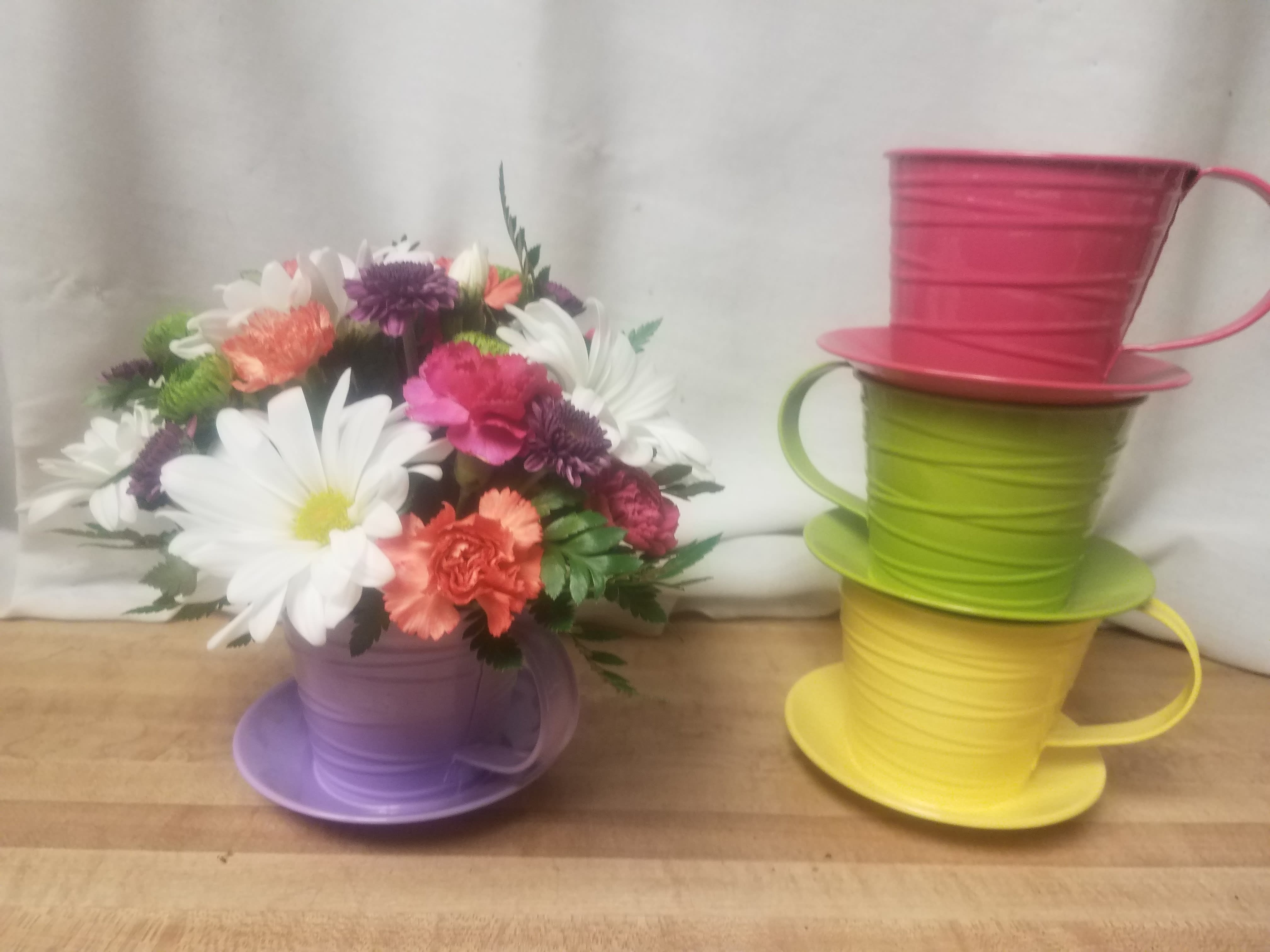 Colorful bouquet in a purple teacup-shaped container beside stacked teacup planters