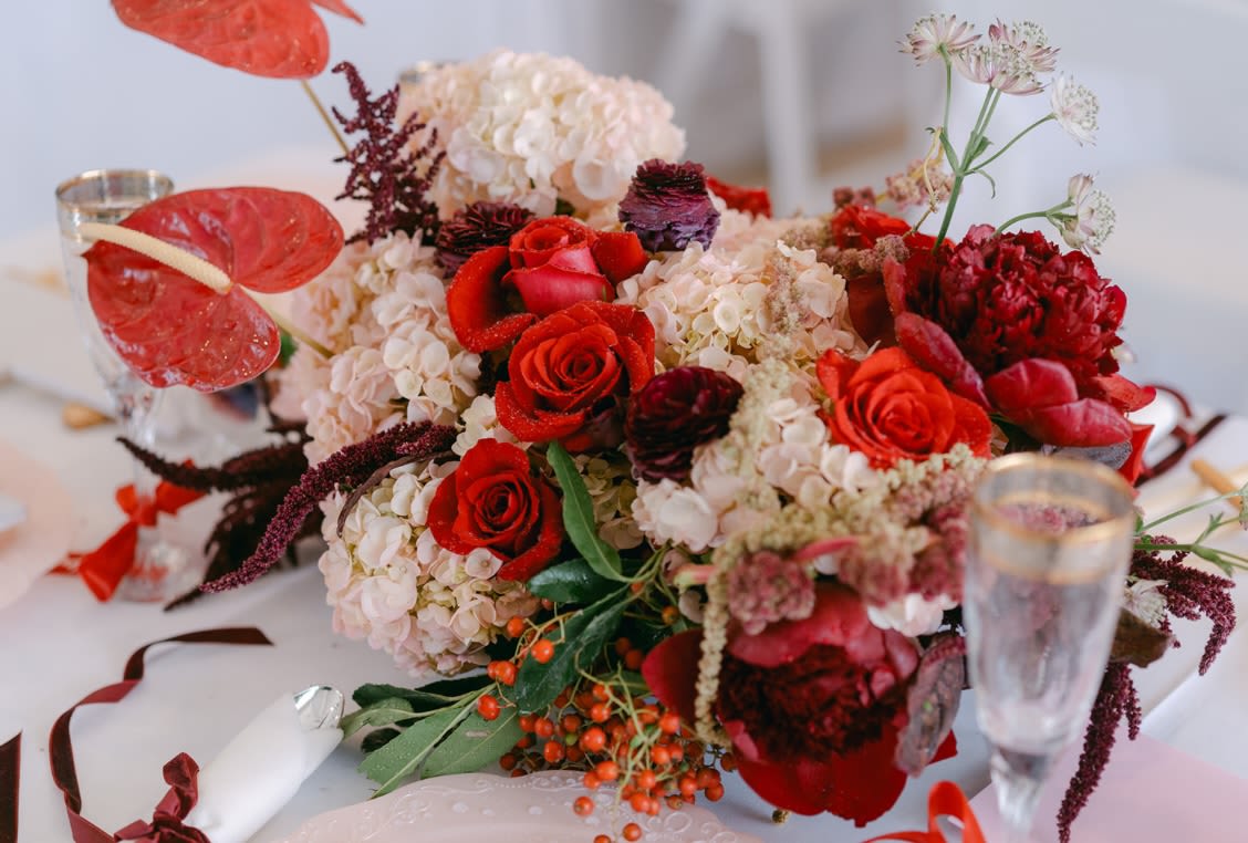 Red roses and pale hydrangeas arranged with anthuriums on a table